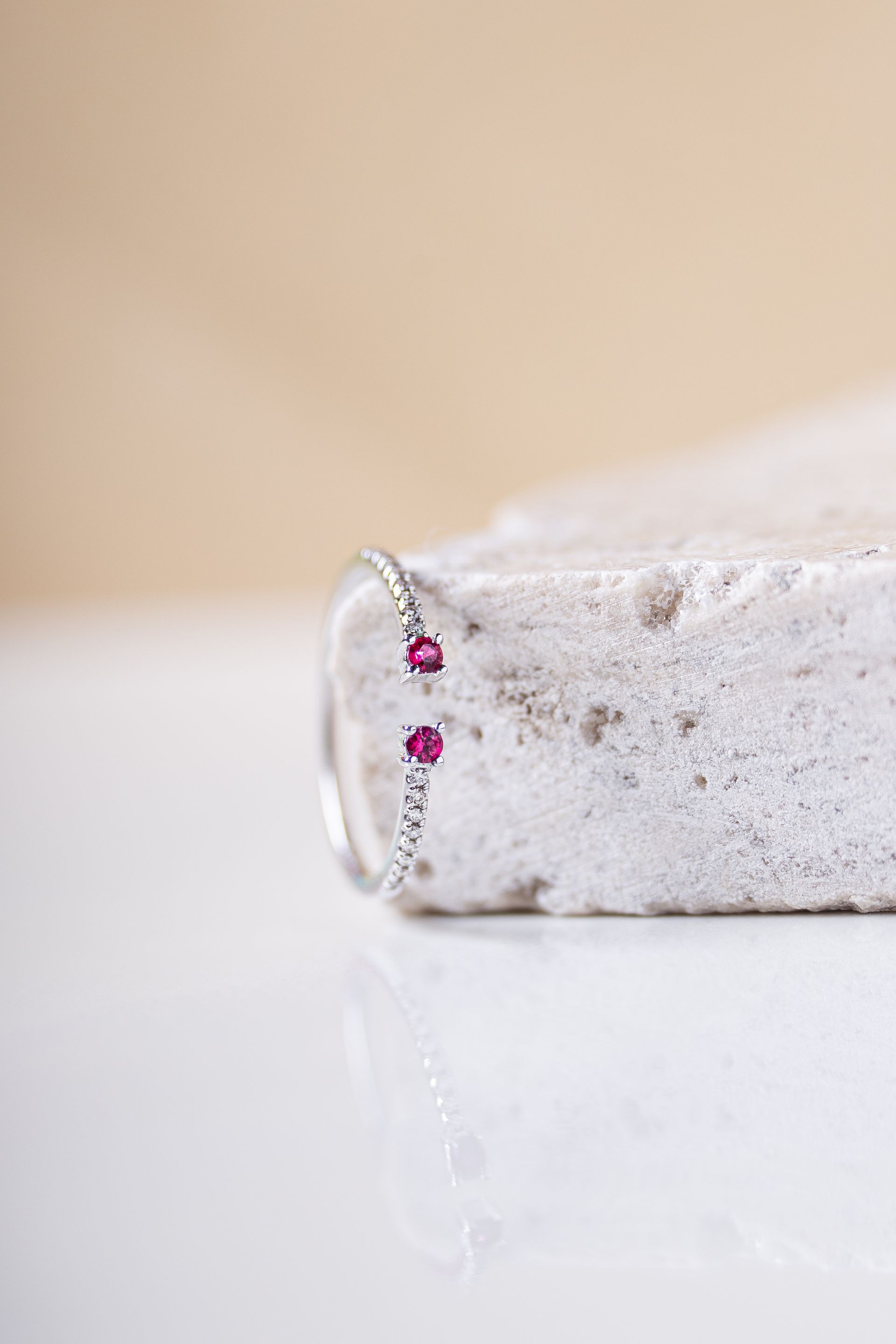 Anillo de plata con dos gemas rosas sobre una superficie blanca texturizada.