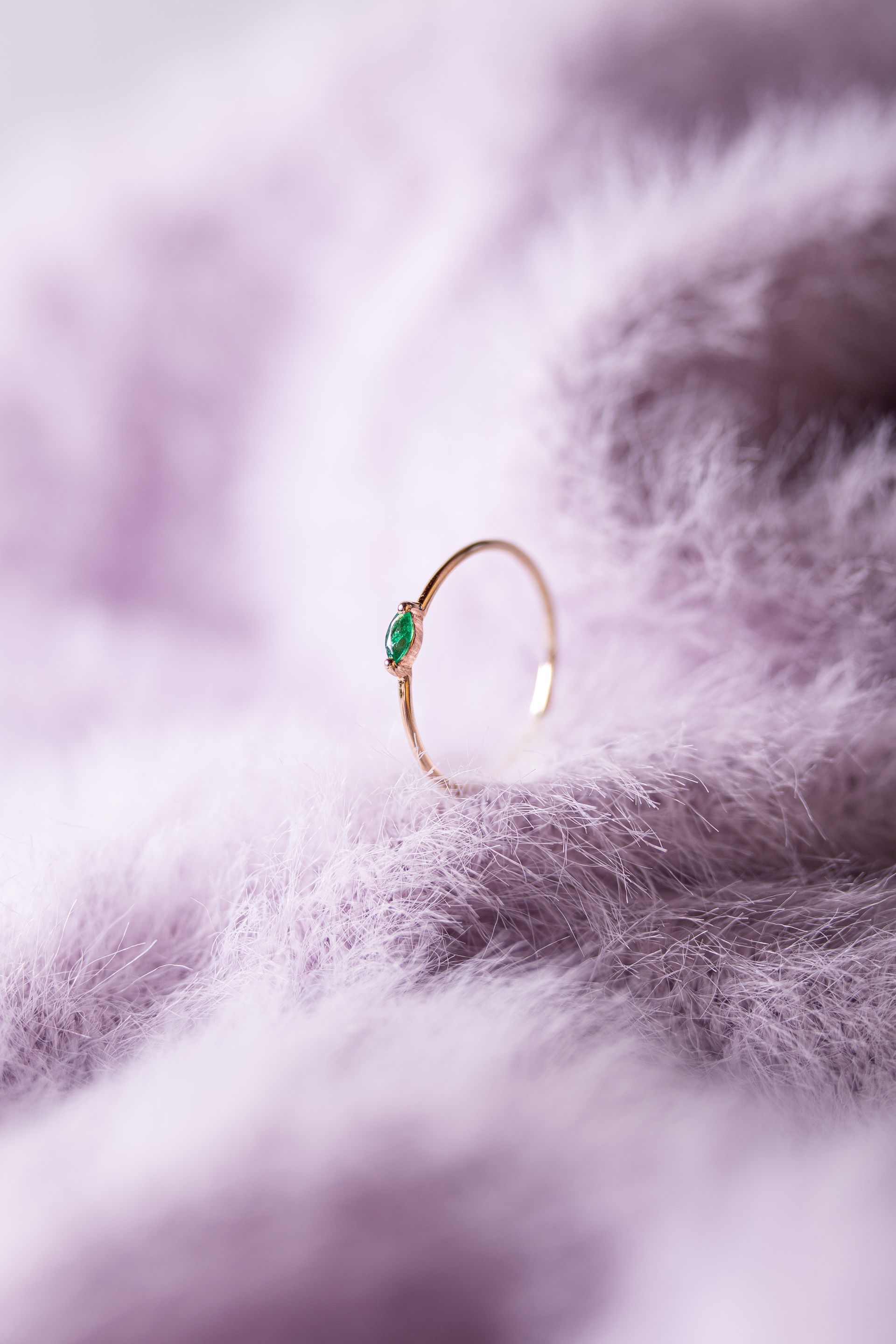 Pendiente de aro dorado con una pequeña piedra preciosa verde sobre una suave piel de color lavanda.