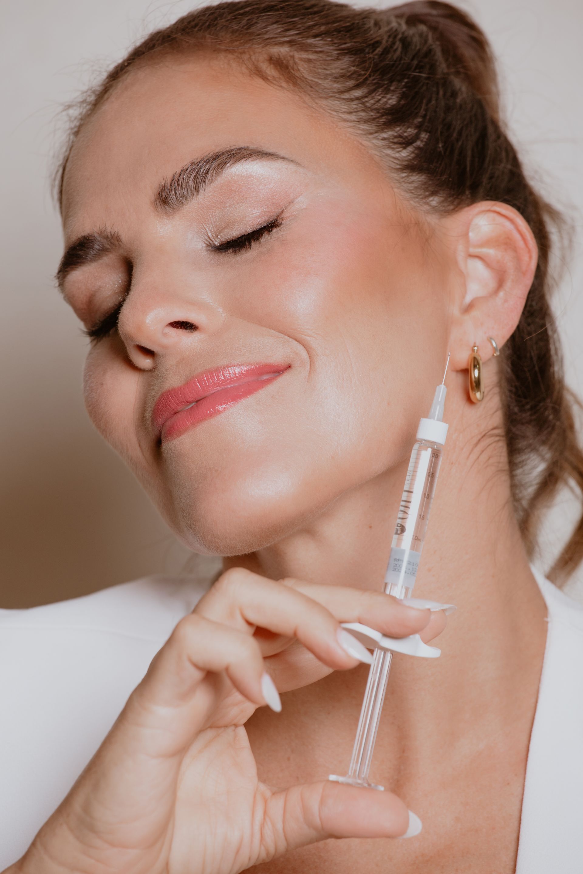 ROM&ROM DOCTORA aplicándose sérum facial con un gotero, con los ojos cerrados, en un retrato de primer plano con iluminación suave.