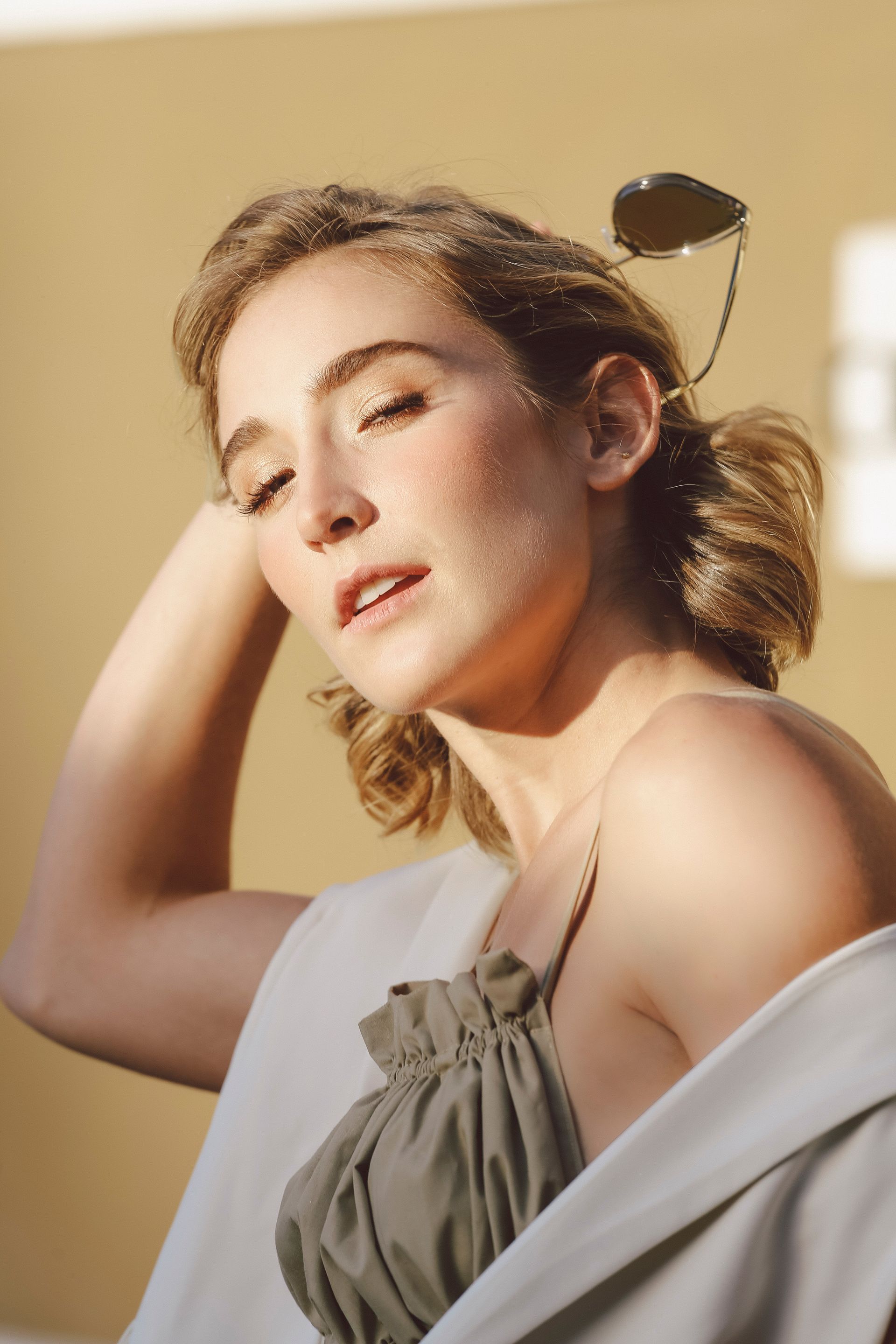 Retrato de una mujer bajo la suave luz del sol, con la mano en el pelo, vestida con una blusa gris y un chal blanco sobre los hombros.
