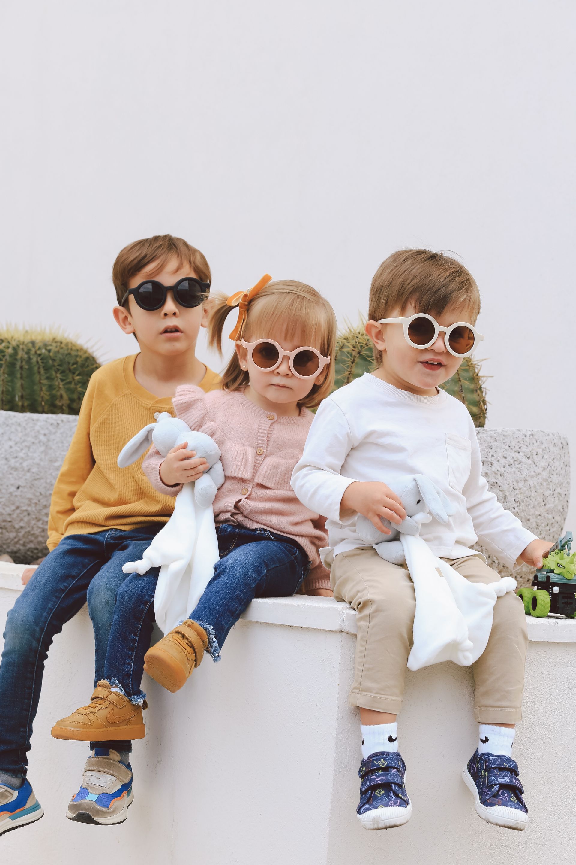 Tres niños con gafas de sol están sentados en un banco al aire libre.