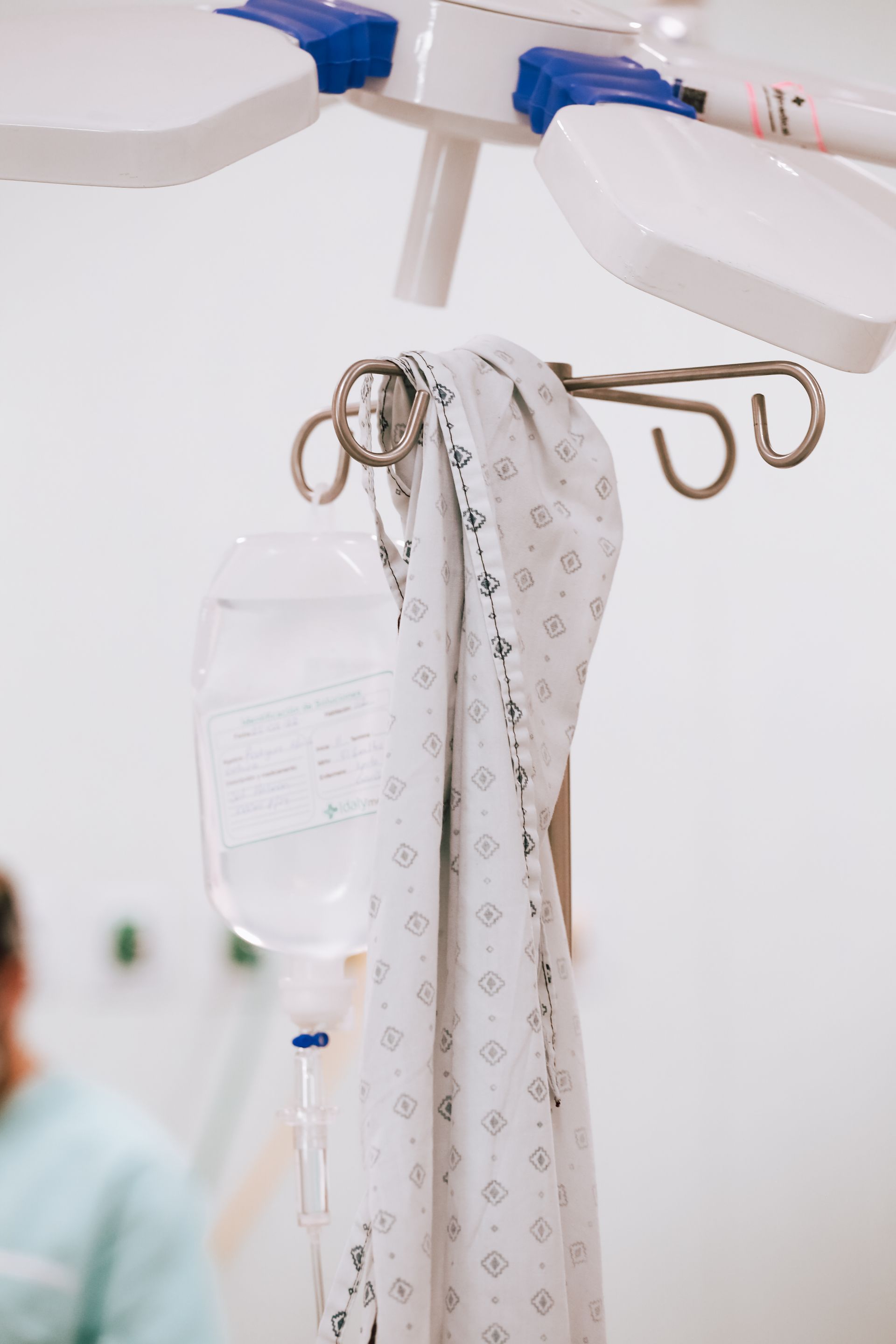 Soporte para suero intravenoso de hospital con papeles médicos colgando y una tela estampada en una habitación clínica.