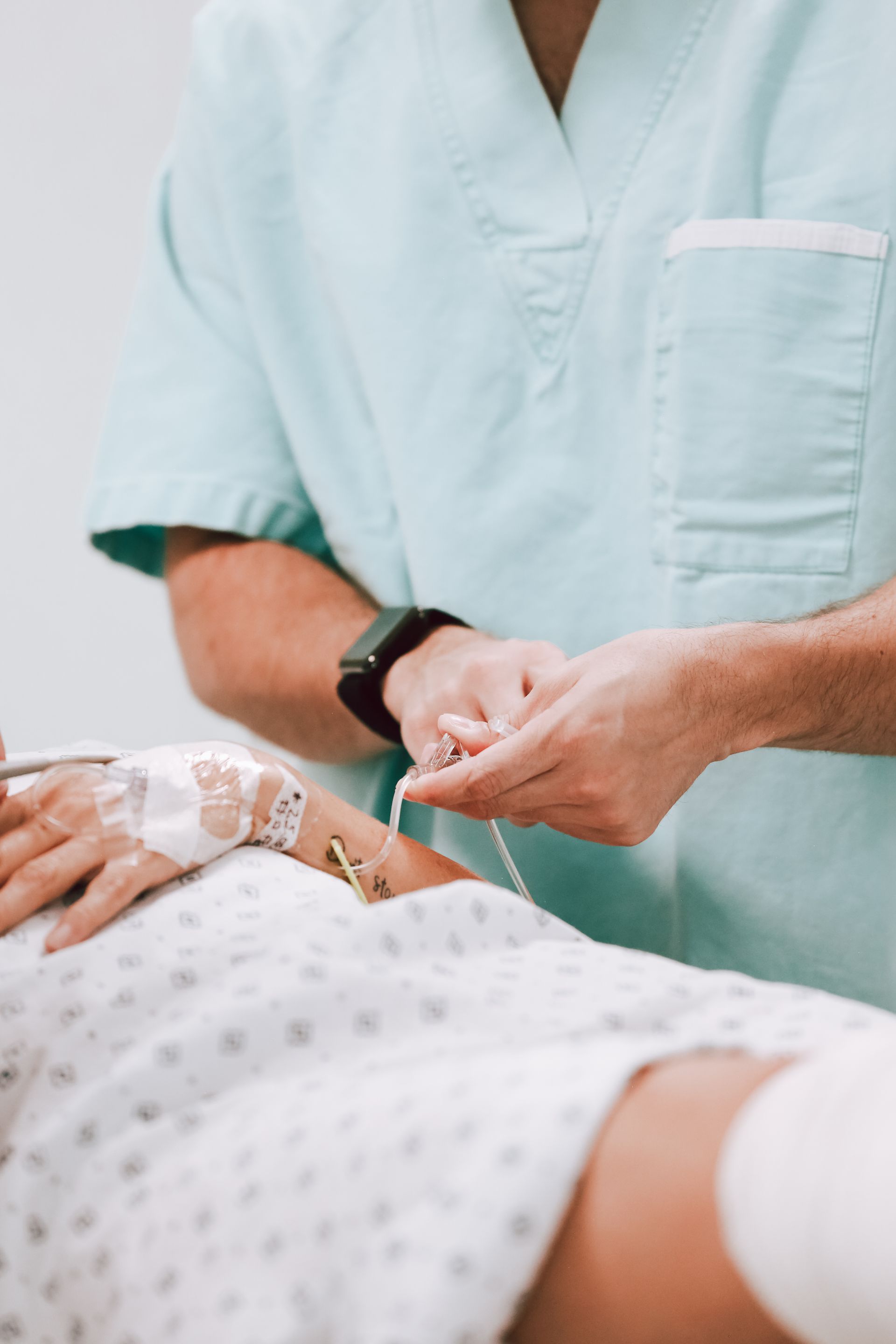 Un trabajador sanitario ajusta una vía intravenosa a un paciente en una cama de hospital.