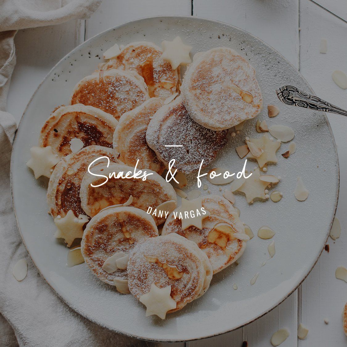 Una pila de rosquillas espolvoreadas con azúcar glas sobre un plato blanco, rodeada de almendras laminadas y granos de café.