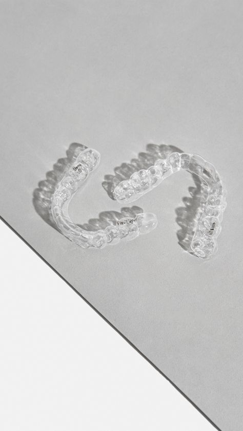 Dos alineadores dentales de plástico transparente y curvado sobre una superficie gris claro.