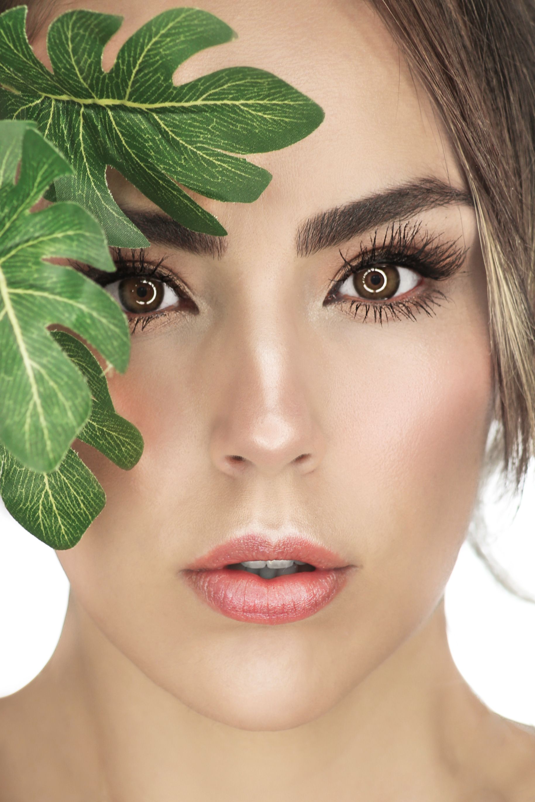 Retrato de cerca de una mujer con hojas verdes que le cubren parcialmente el rostro.