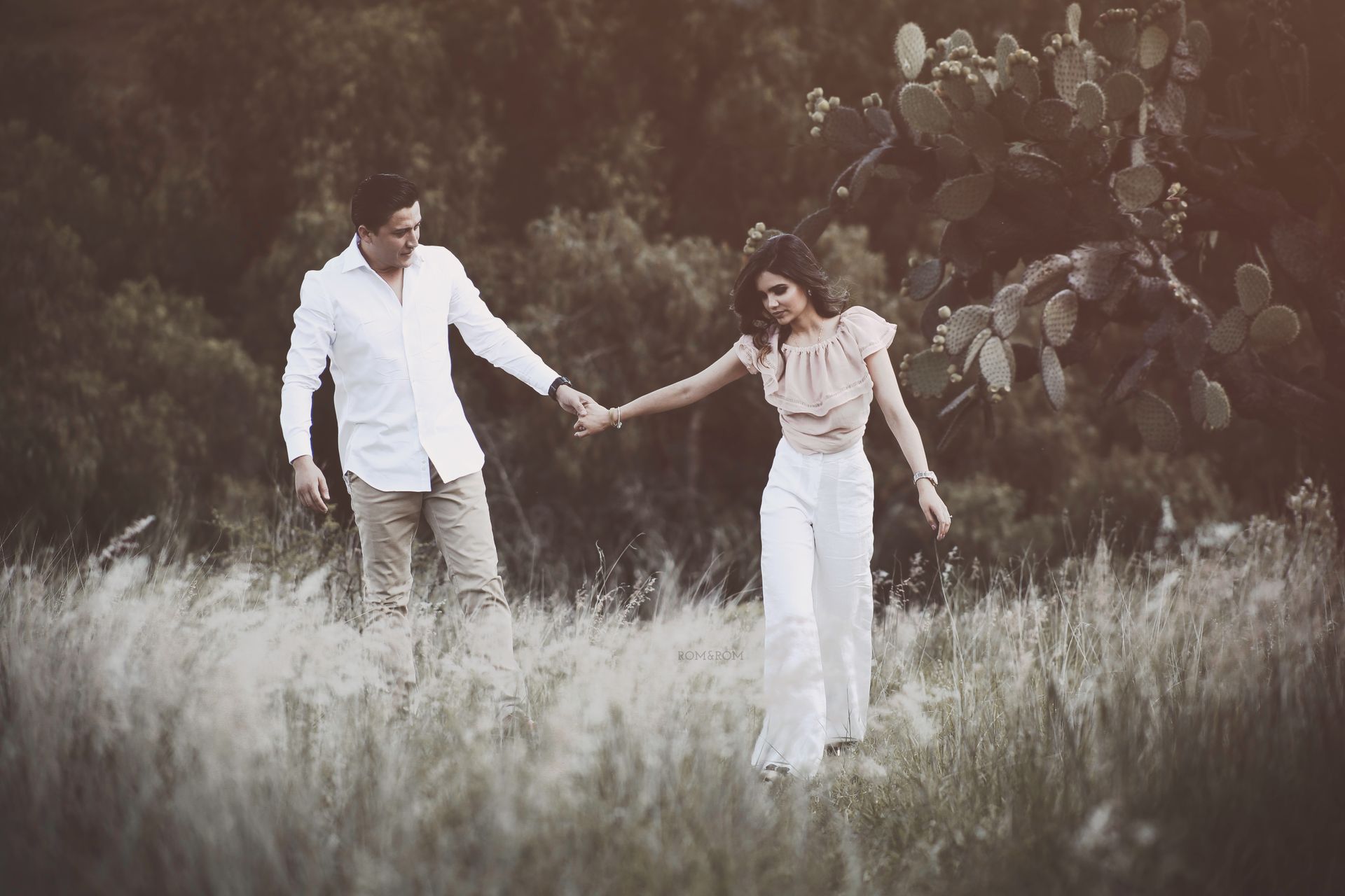 Una pareja camina de la mano por un campo de hierba, con árboles al fondo.