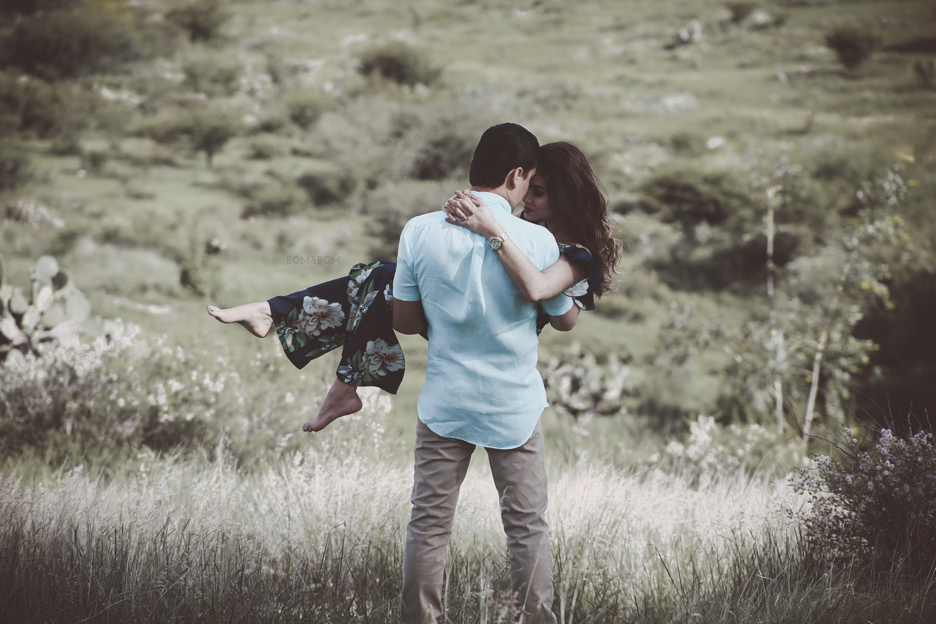 Una pareja se abraza en un campo de hierba, con una persona levantada del suelo.