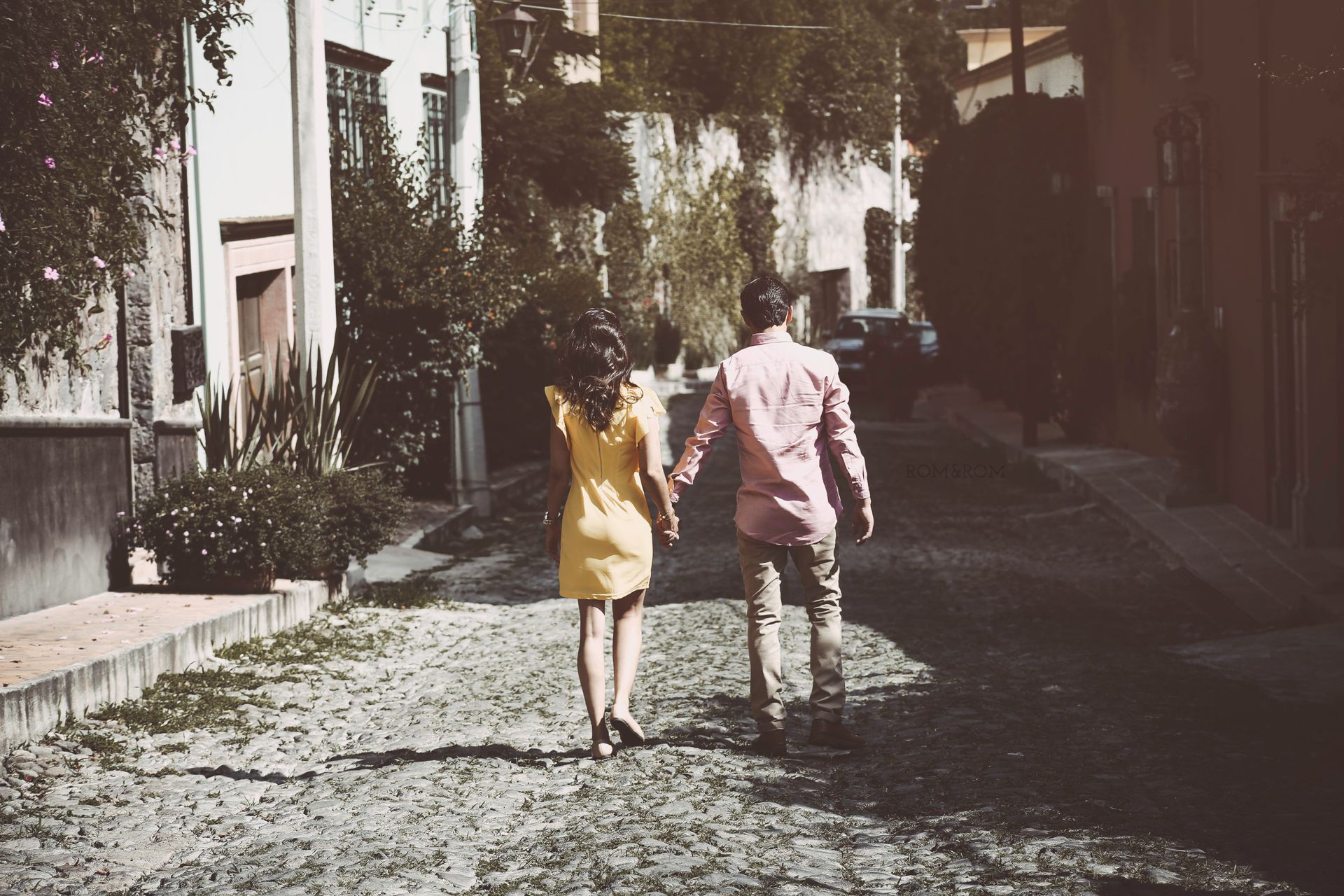 Dos personas caminando de la mano por una calle empedrada iluminada por el sol.