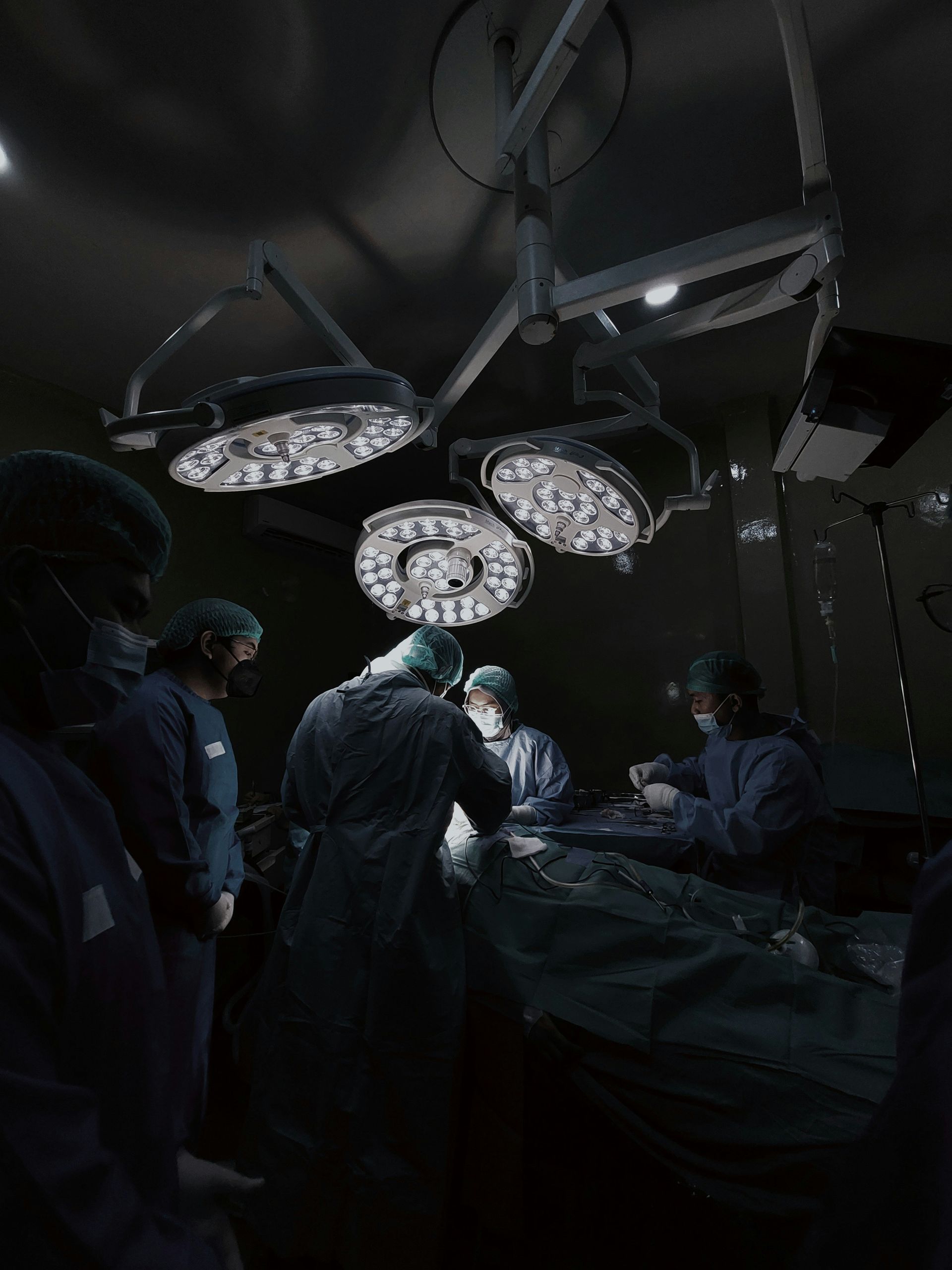 Equipo quirúrgico en un quirófano con poca luz, reunido alrededor de un paciente bajo las brillantes luces del techo.
