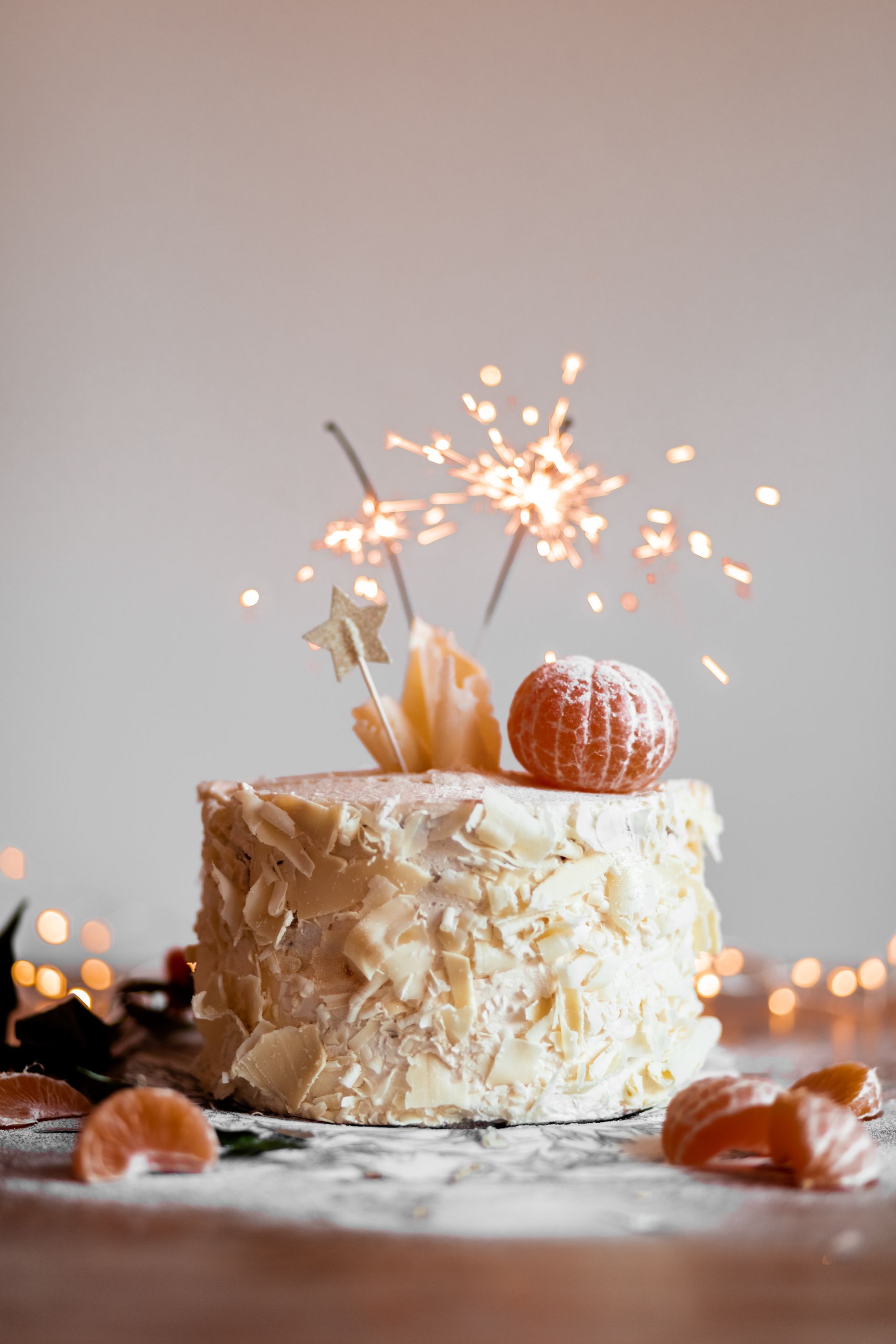 Pastel con bengala y decoración de calabaza naranja sobre una mesa blanca, con cálidas luces bokeh de fondo.