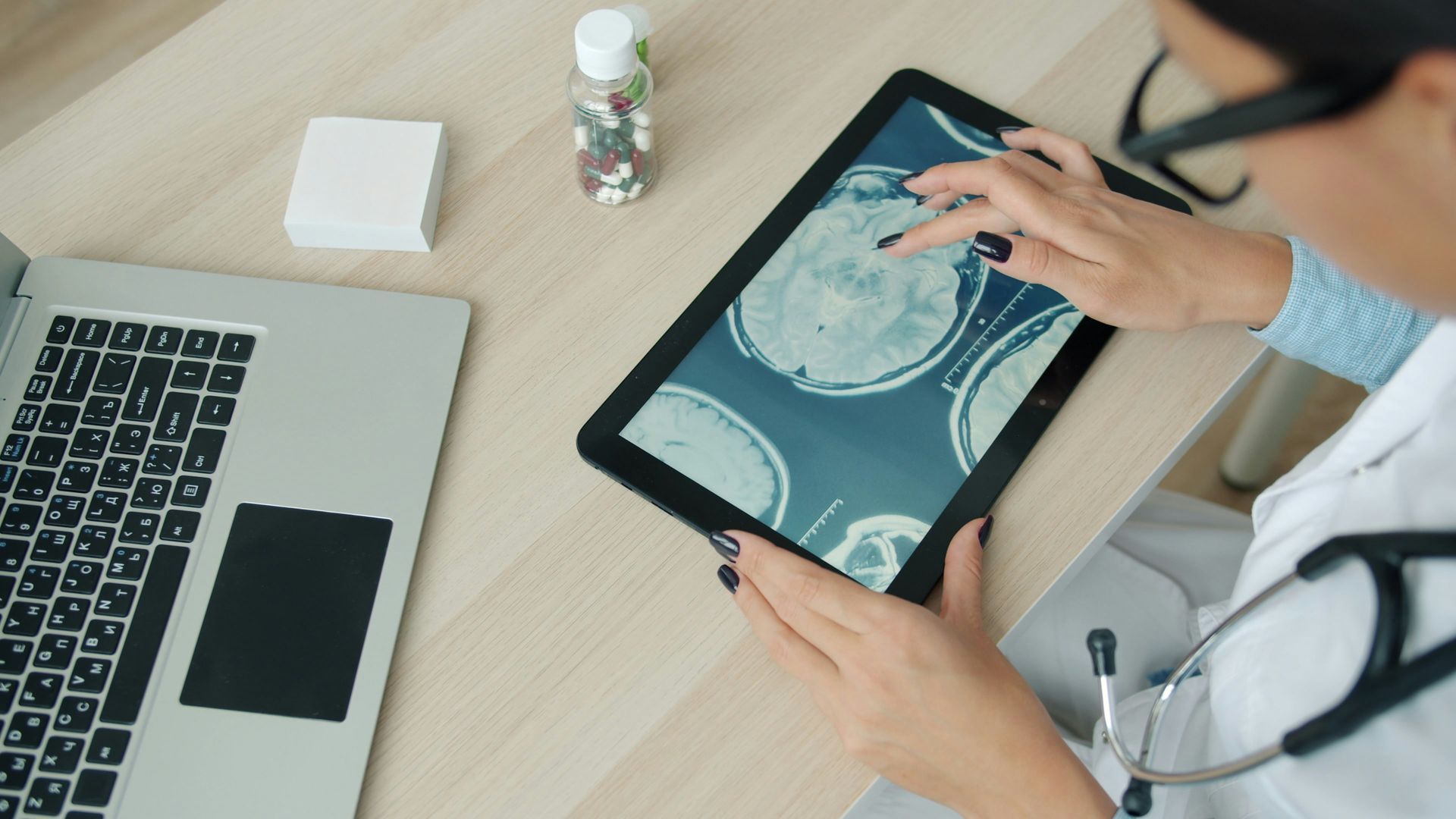 Un médico revisa una radiografía en una tableta junto a una computadora portátil en un escritorio.