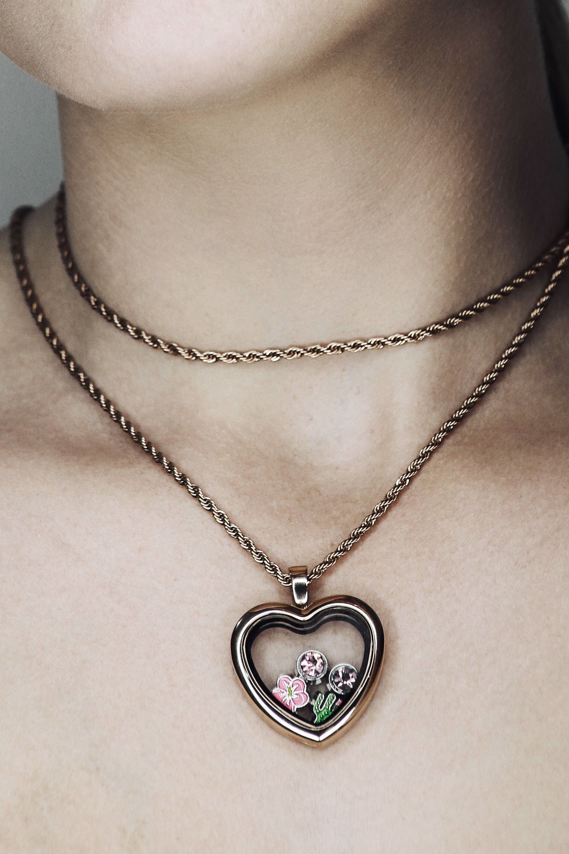 Dos collares de oro superpuestos, uno de ellos con un colgante en forma de corazón que sostiene flores rosas.