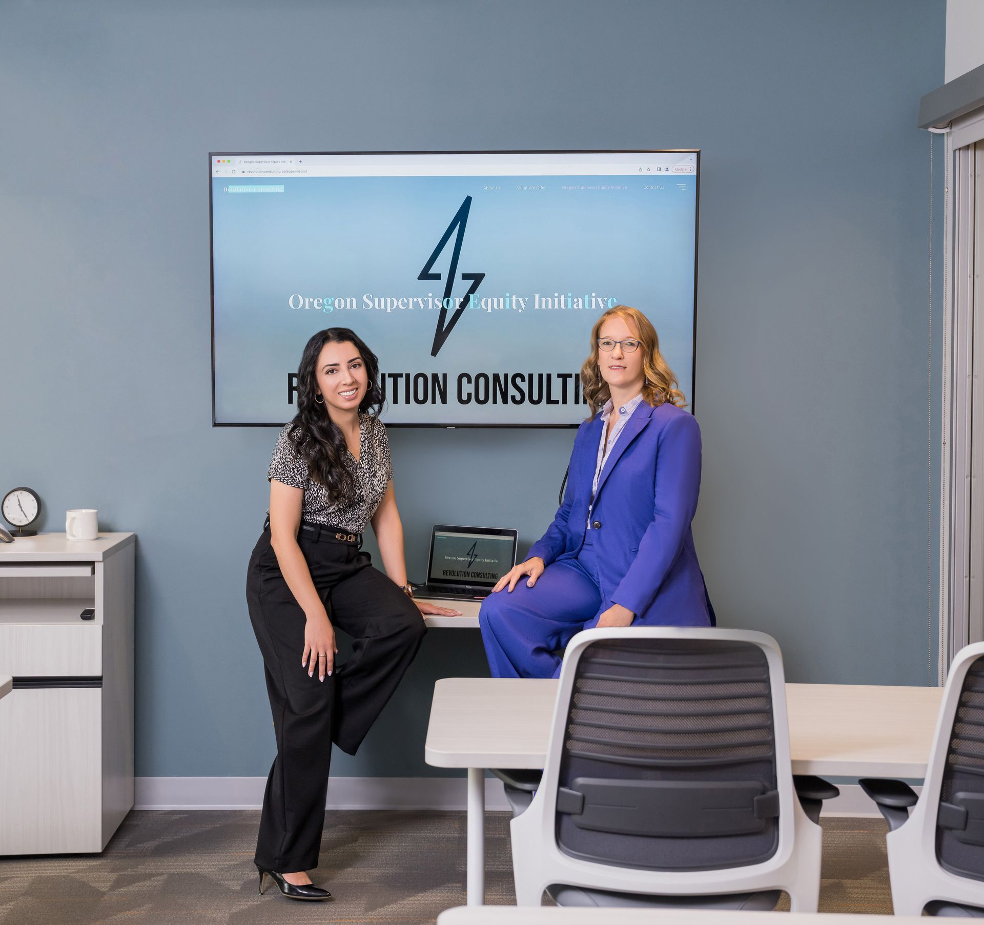 Anjabeen and Arien are posing for a picture in front of a sign that says Revolution Consulting