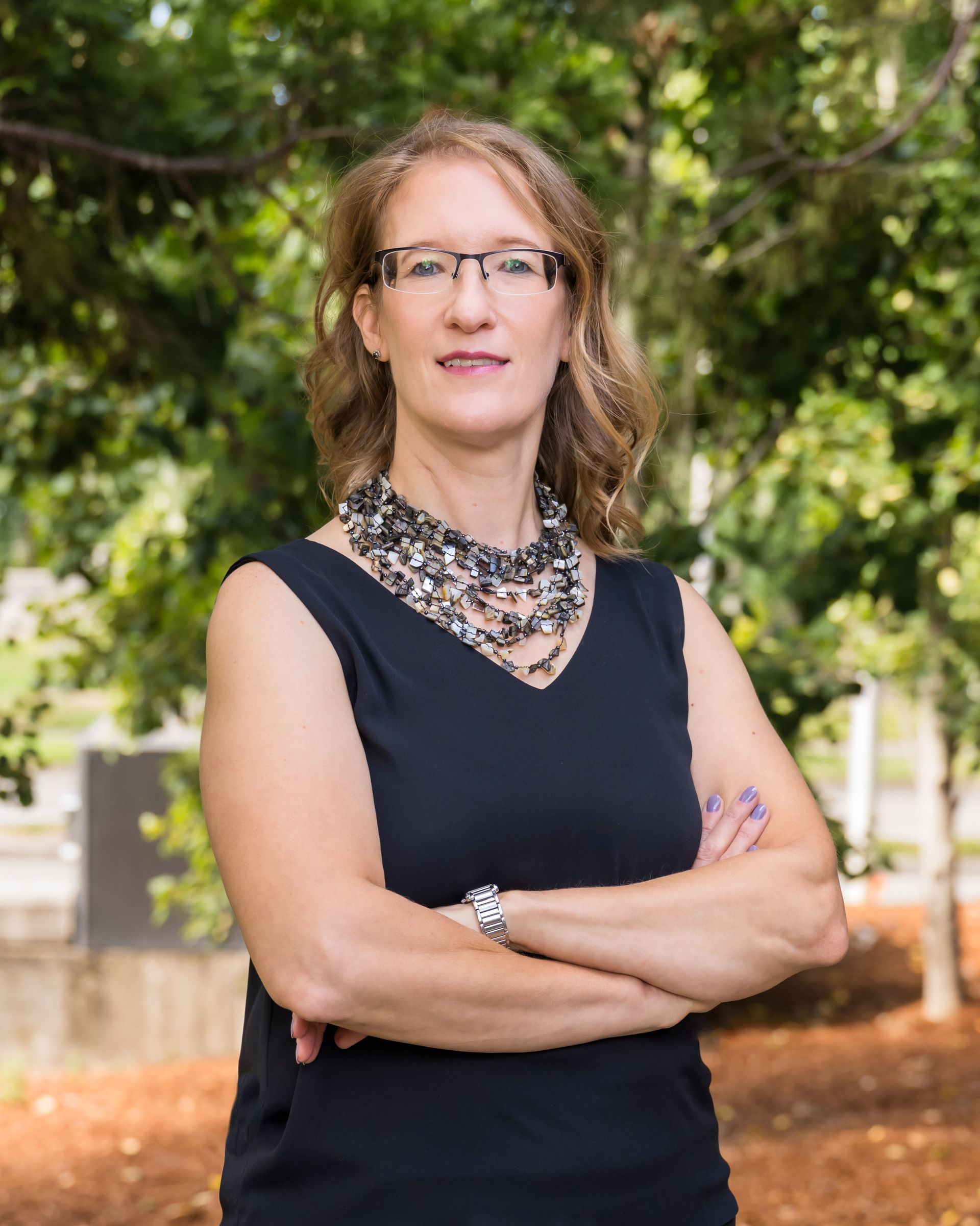 Arien, wearing glasses and a black tank top, is standing with her arms crossed.
