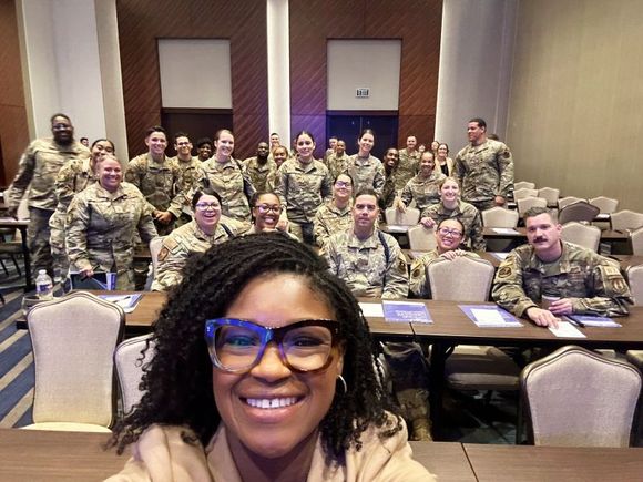 A woman is taking a selfie with a group of soldiers in a conference room.