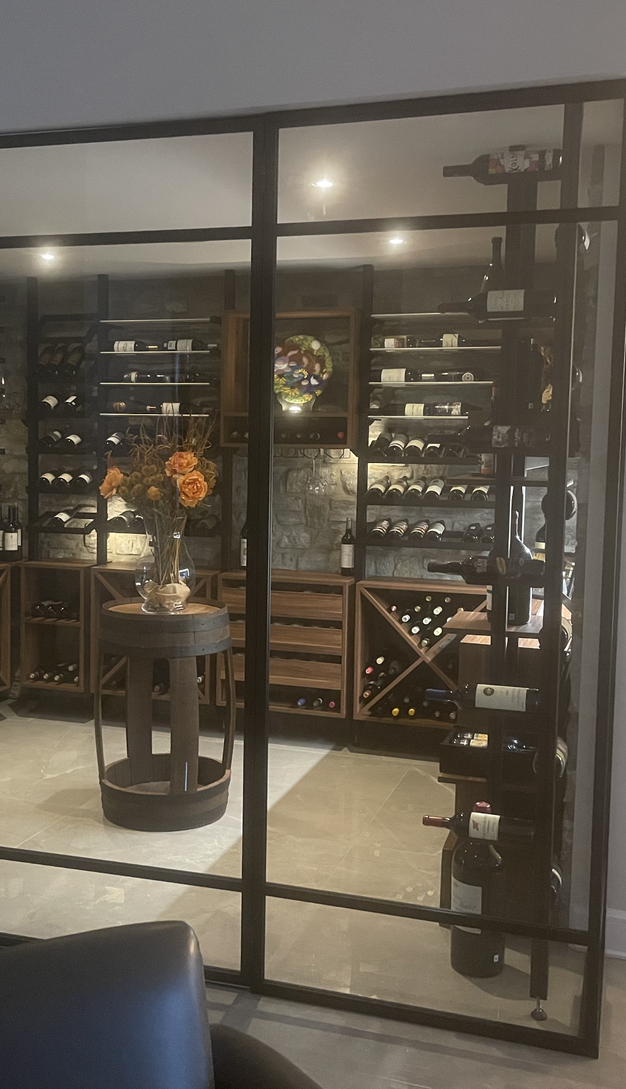 Cave à vin avec portes vitrées, dotée d'étagères en bois, de murs en pierre et d'une table à tonneaux.