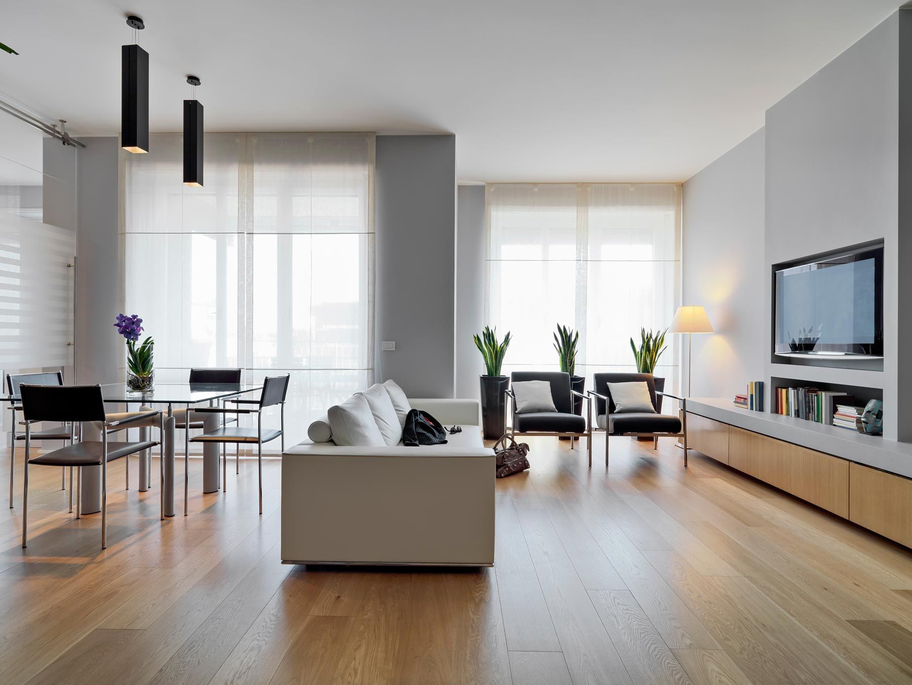 Salon moderne avec parquet, murs gris, canapé blanc, coin repas et télévision.