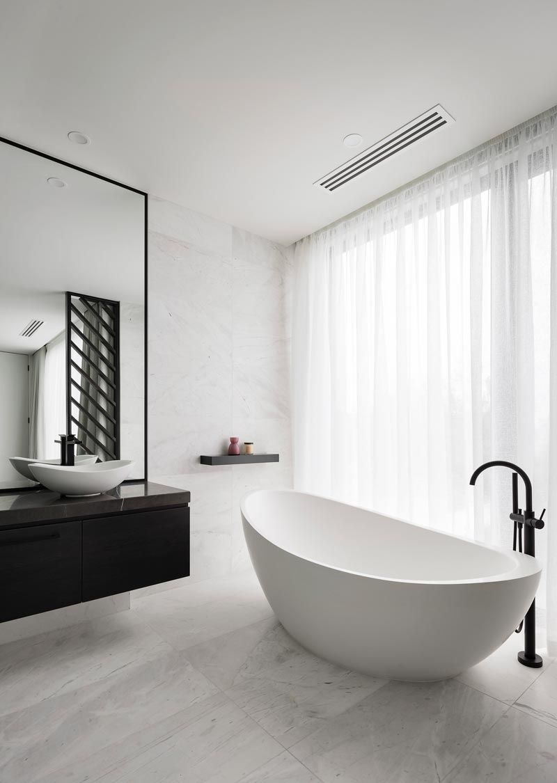 Salle de bain blanche moderne avec une baignoire ovale autoportante, une vanité noire, un grand miroir et des rideaux blancs transparents.