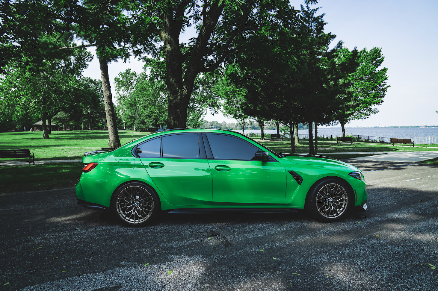 A green bmw m3 is parked in a parking lot surrounded by trees.