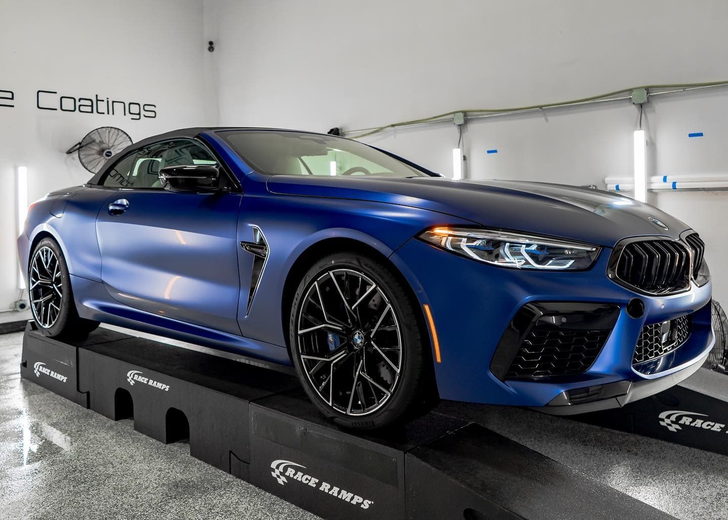 A blue bmw m8 convertible is parked on a ramp in a garage.