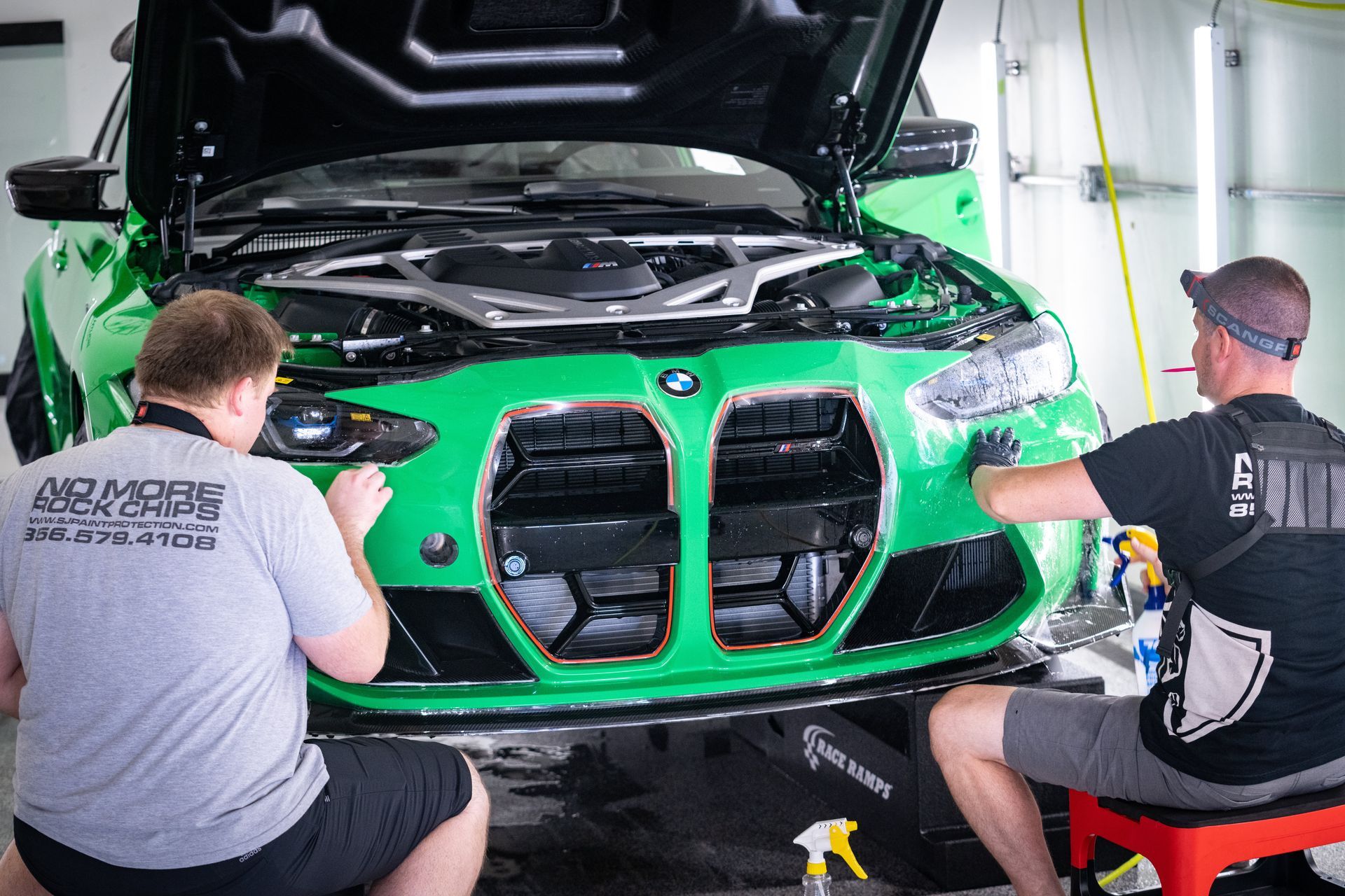 Two men are working on the front of a green bmw m4.