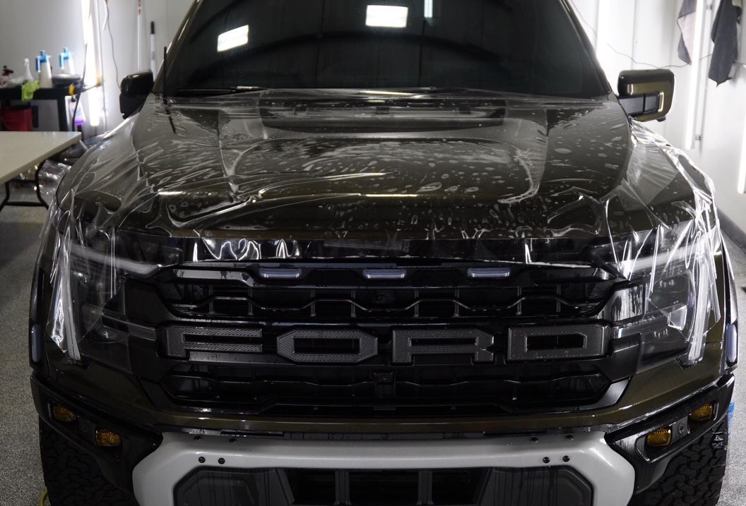 A black ford raptor is wrapped in plastic in a garage.