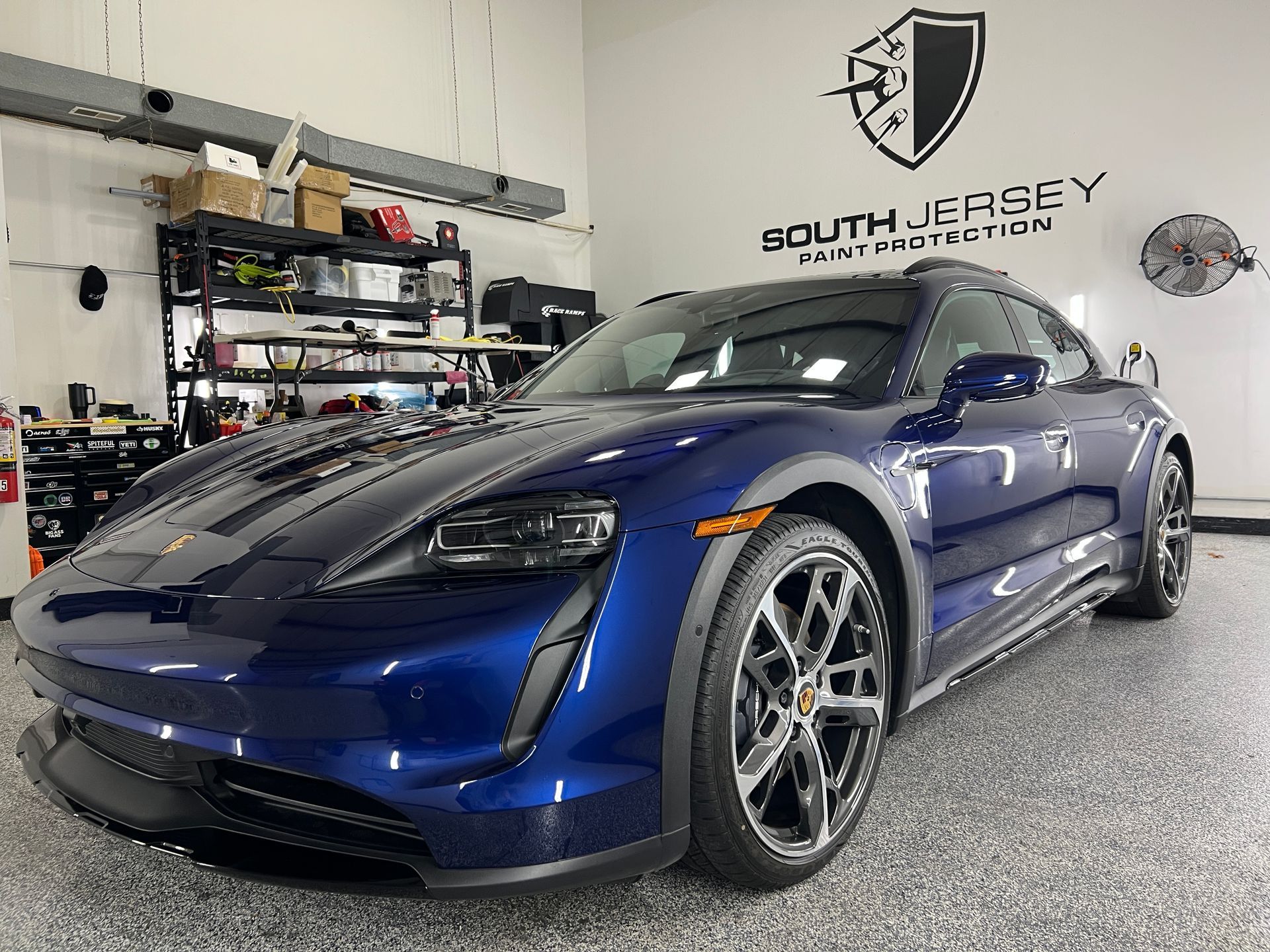 A blue porsche taycan turbo s is parked in a garage.