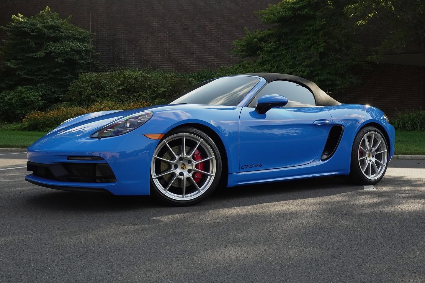 Blue sports car parked outdoors on asphalt with a black roof and silver wheels