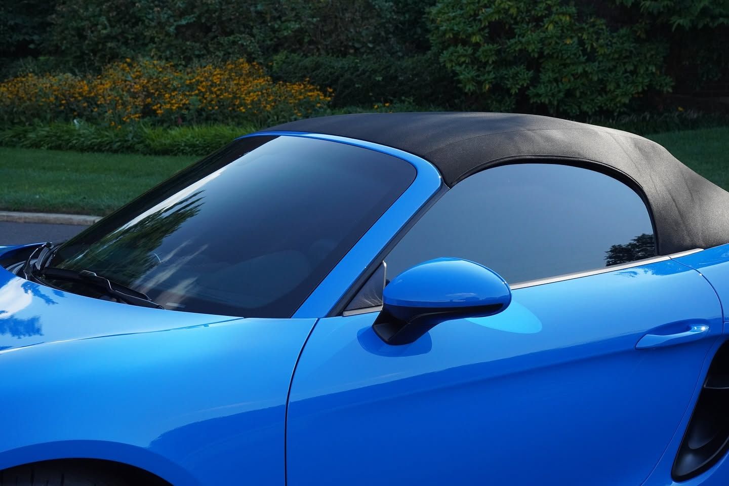 Blue convertible sports car with black soft top parked outdoors near greenery