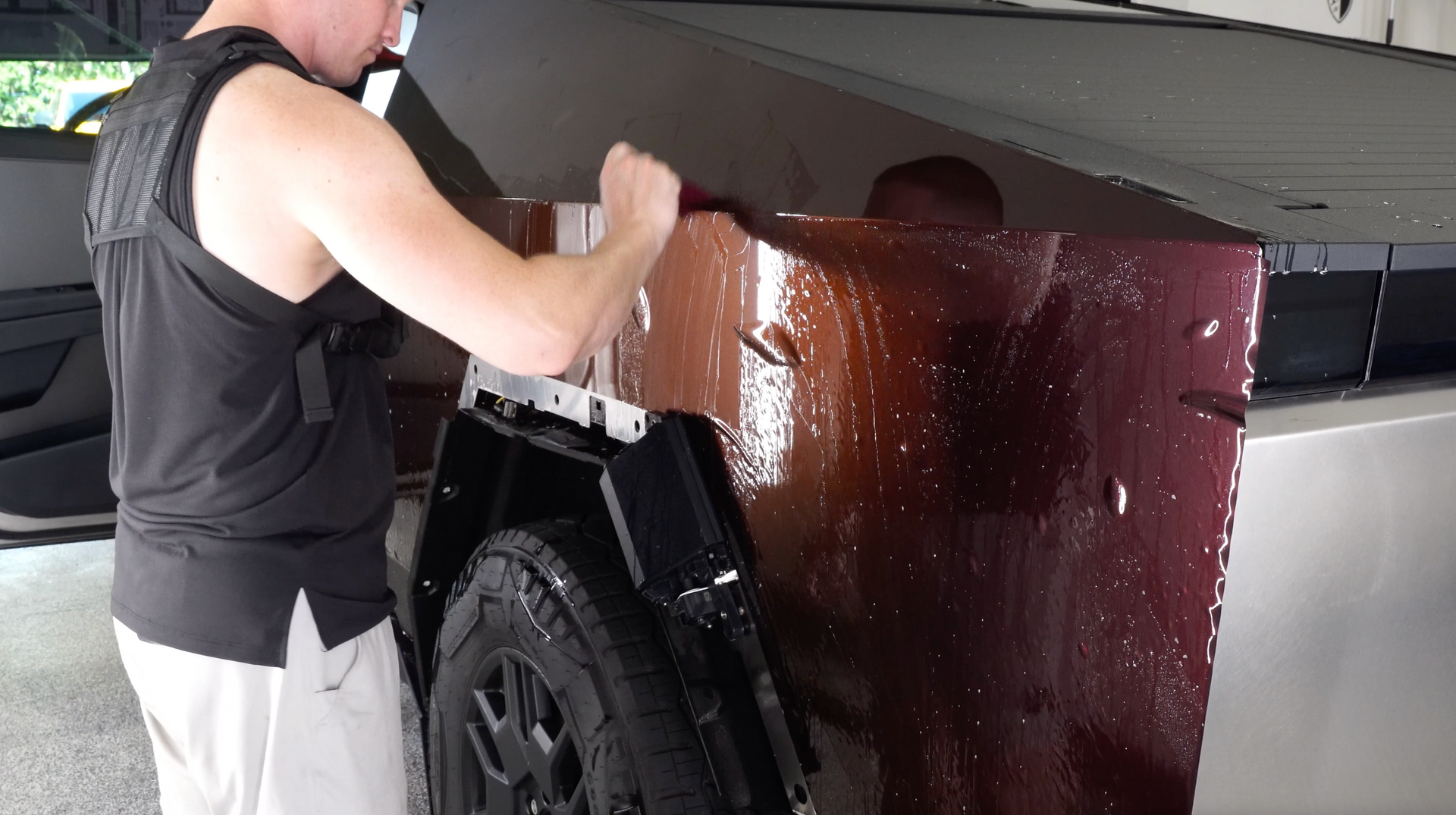 A man in a black tank top is working on a car.
