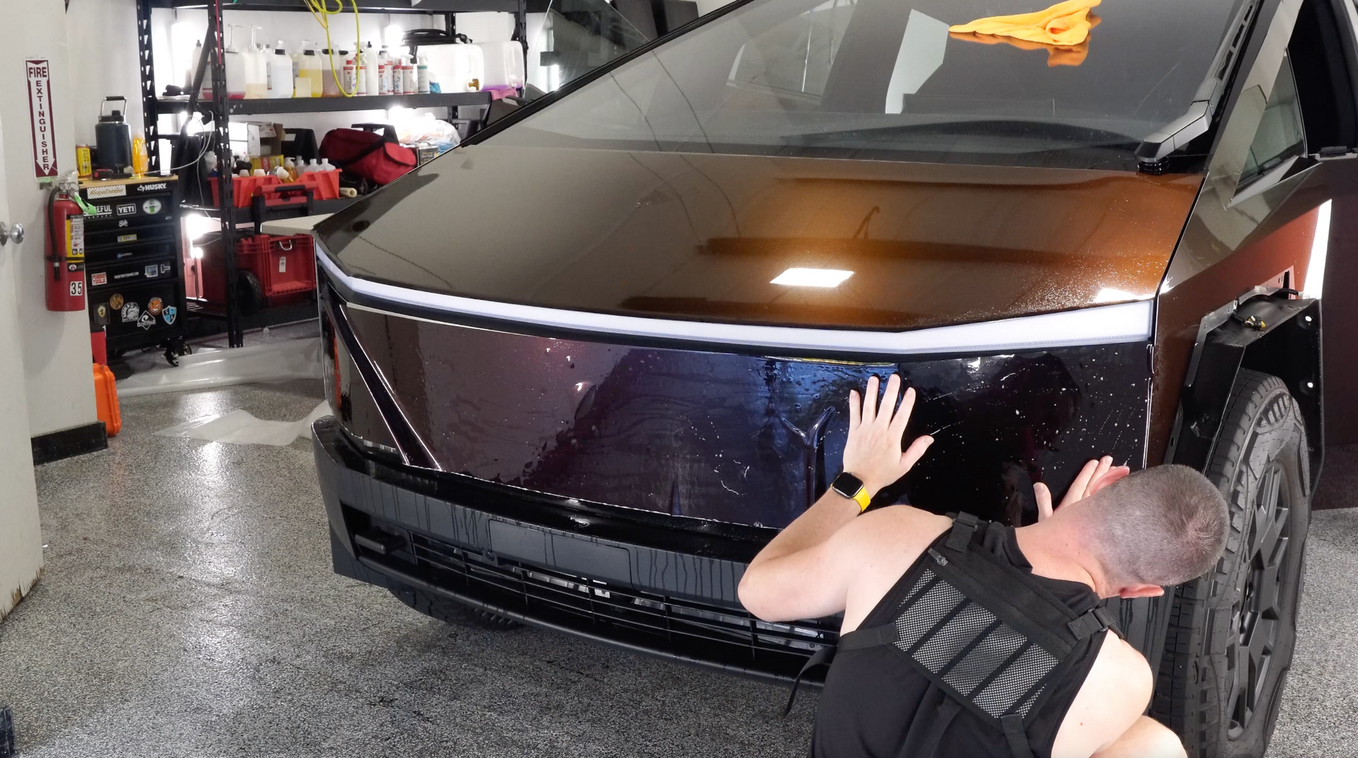 A man is kneeling down in front of an electric car in a garage.