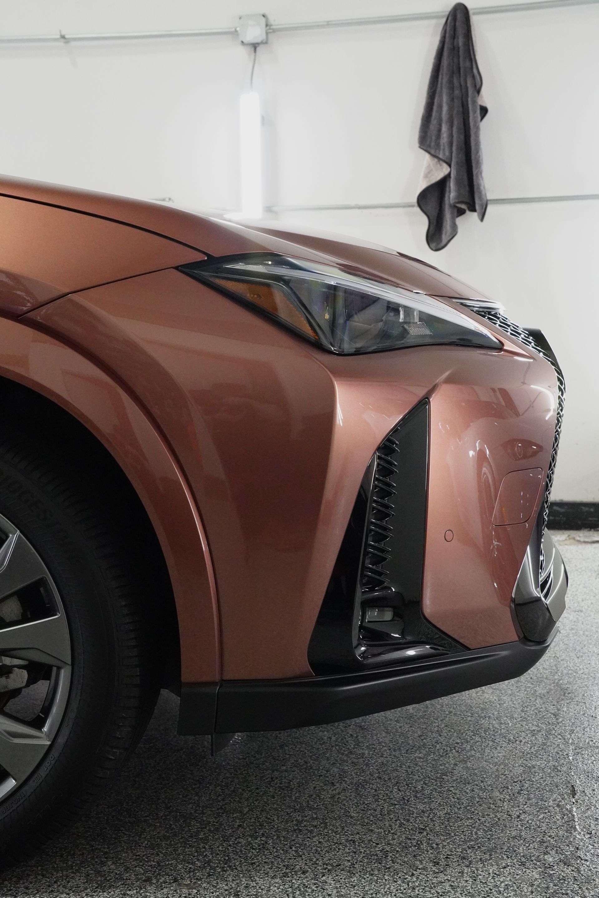 A brown car is parked in a garage with a towel hanging on the wall.