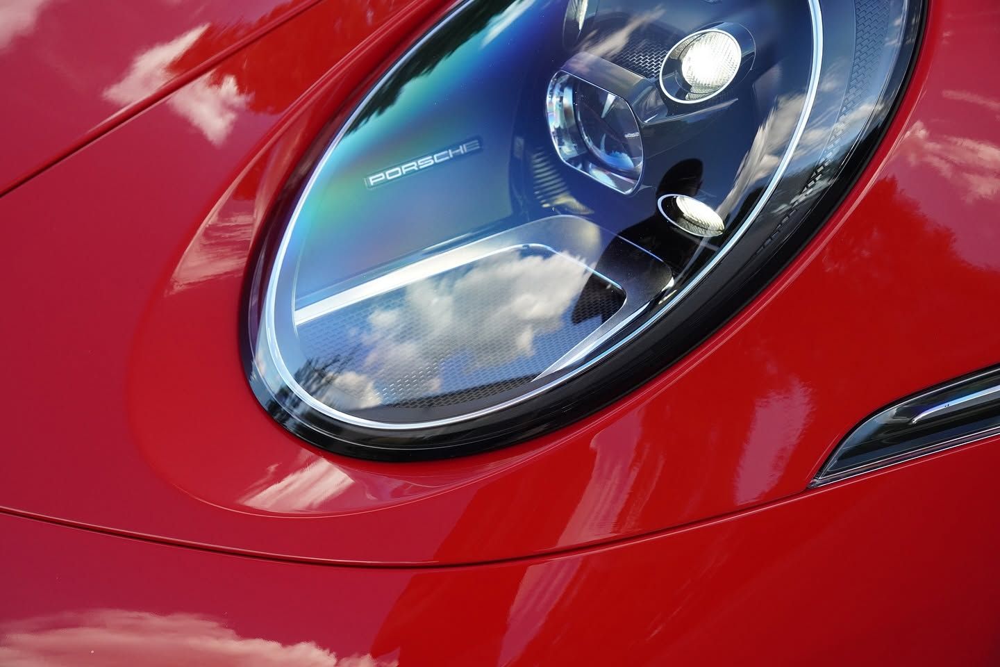 Close-up of a red sports car headlight with sky reflections