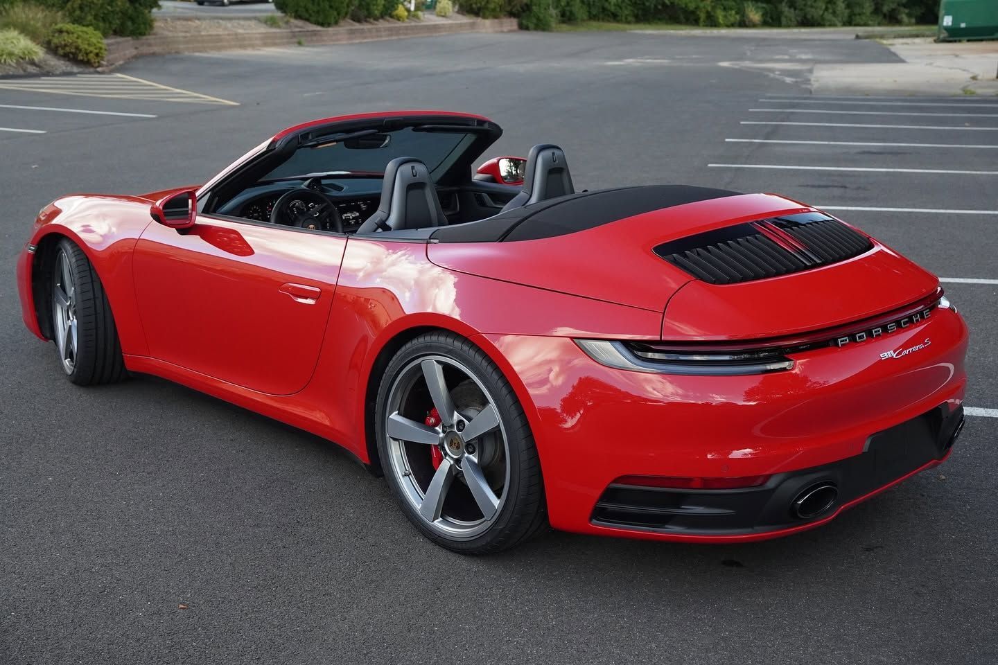 Red sports car parked in a lot, rear three-quarter view, with black roof and silver wheels