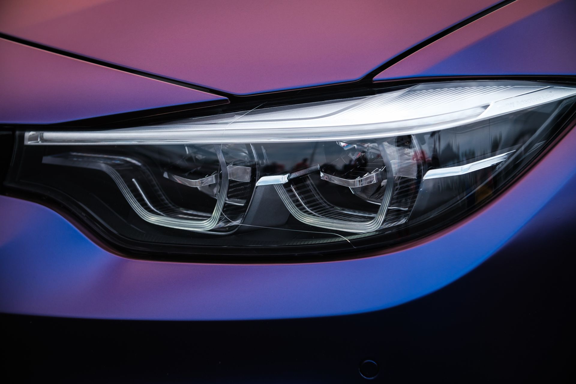 Close-up of a sleek car headlight on a purple and black vehicle front