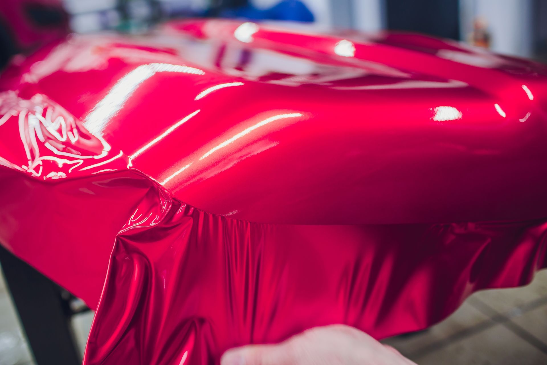 Close-up of a glossy red car being wrapped in vinyl film by gloved hands