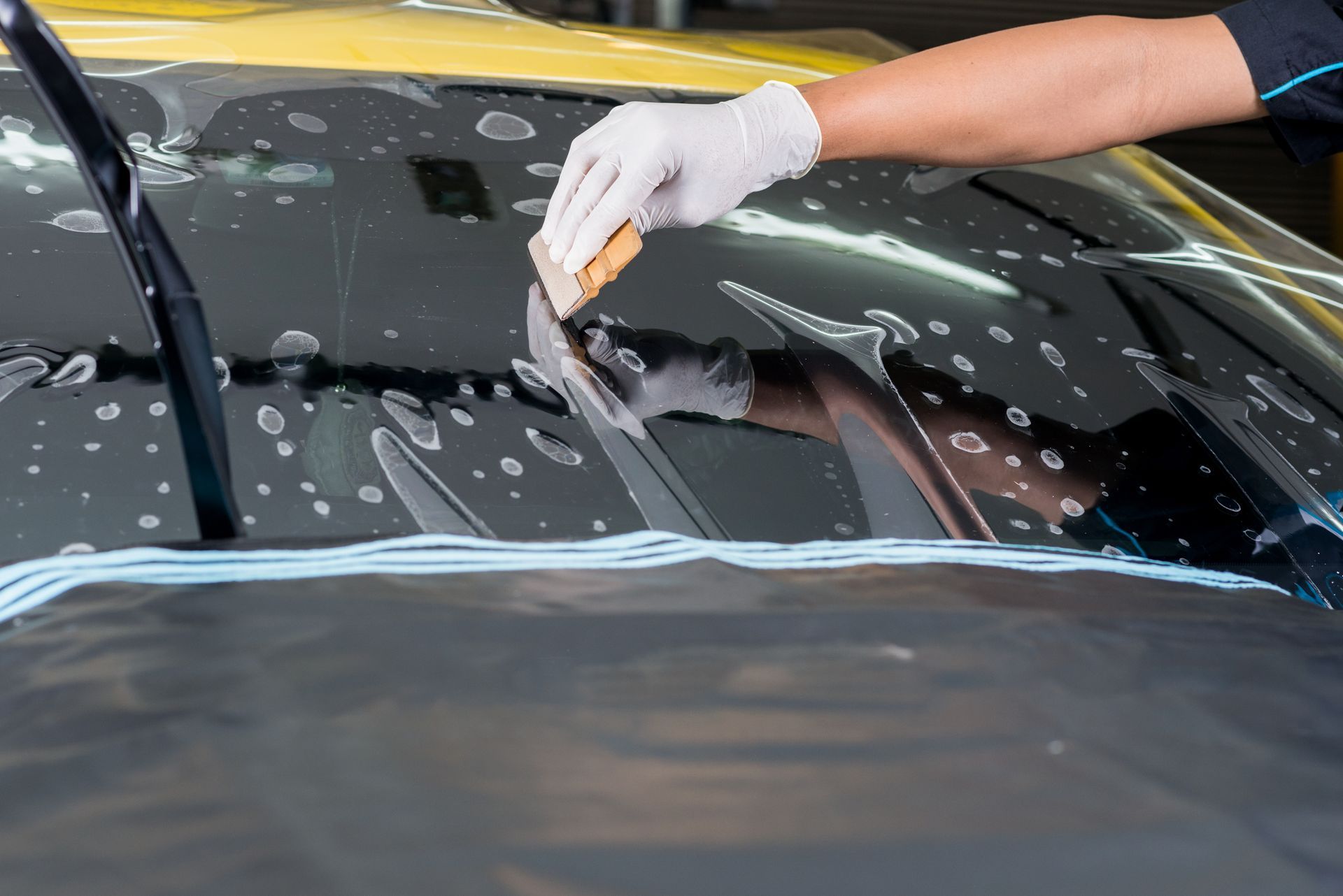 Gloved hand scrapes soap off a black car windshield during washing