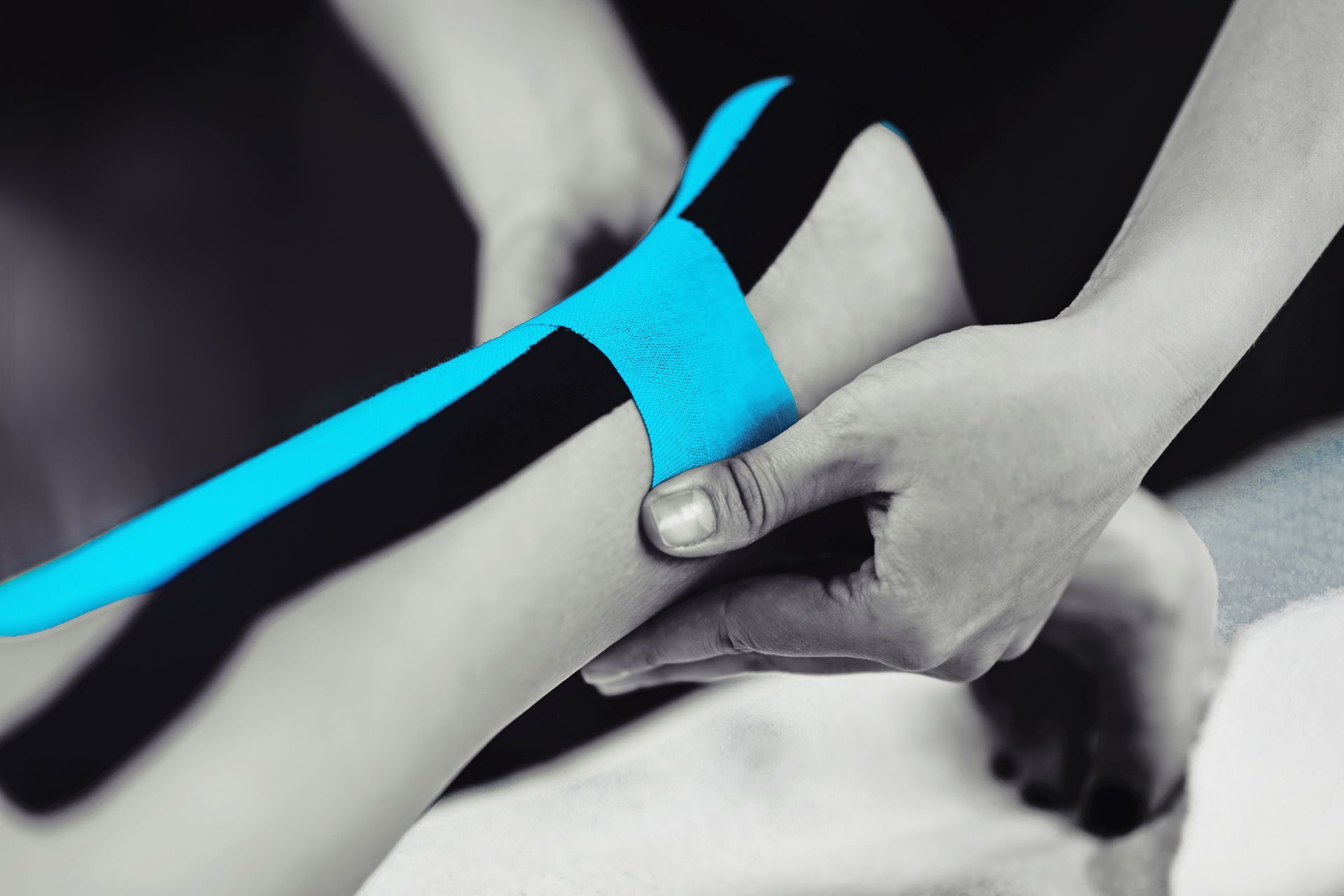 Person applying blue and black kinesiology tape to an ankle.