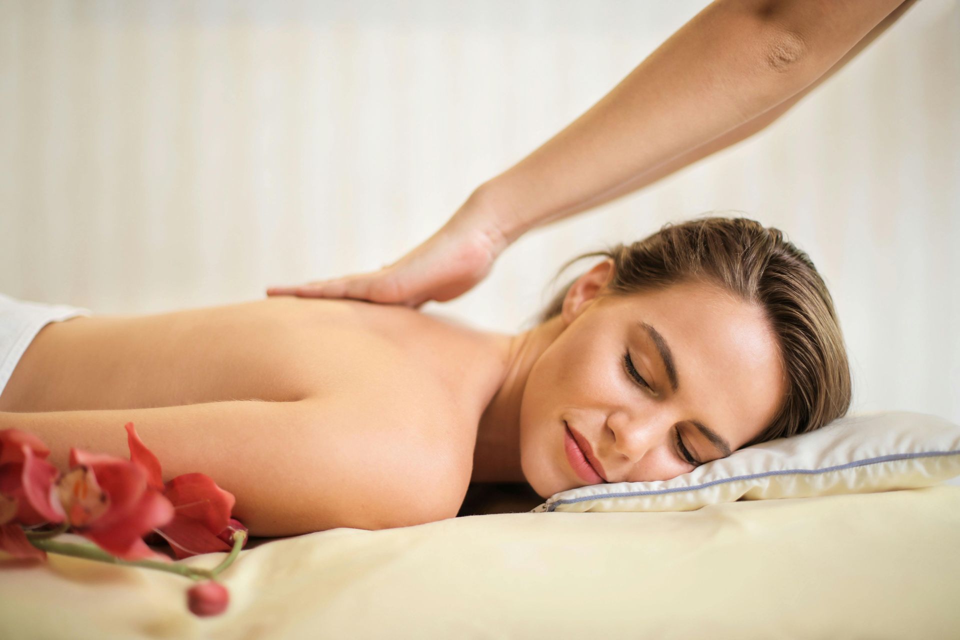 Woman receiving a massage, lying face down on a massage table. A hand presses on her back.