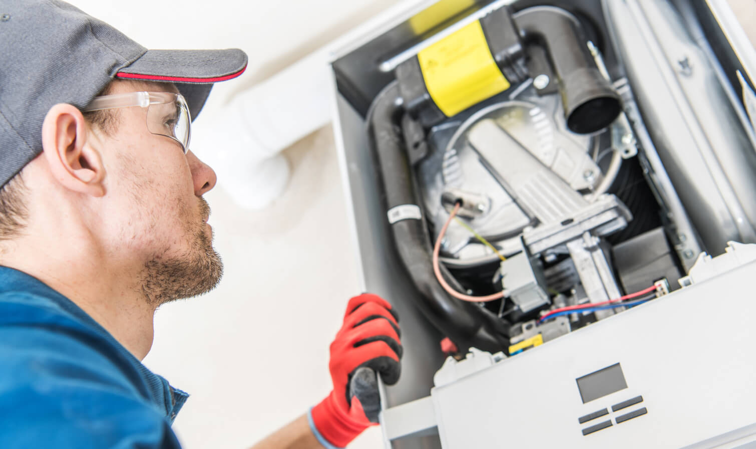 HVAC technician inspecting a furnace, wearing gloves and safety glasses in a home.