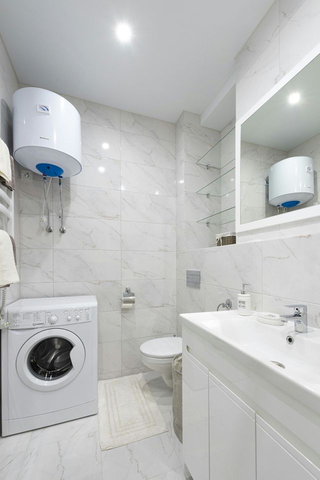 White bathroom with washer, toilet, sink, water heater, and large mirror.