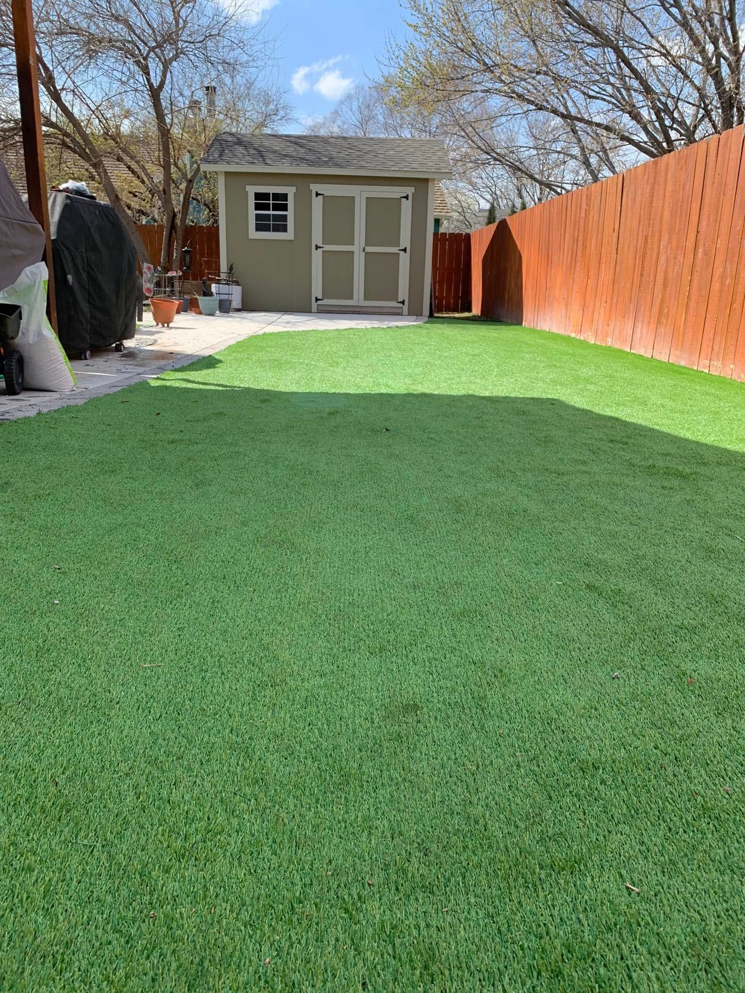 Green artificial turf backyard with a shed and a red fence.