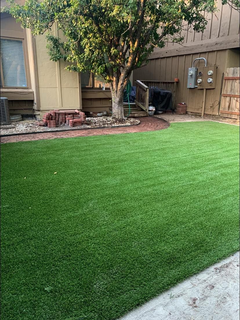 Backyard with vibrant green artificial turf, tree, and wooden fence.