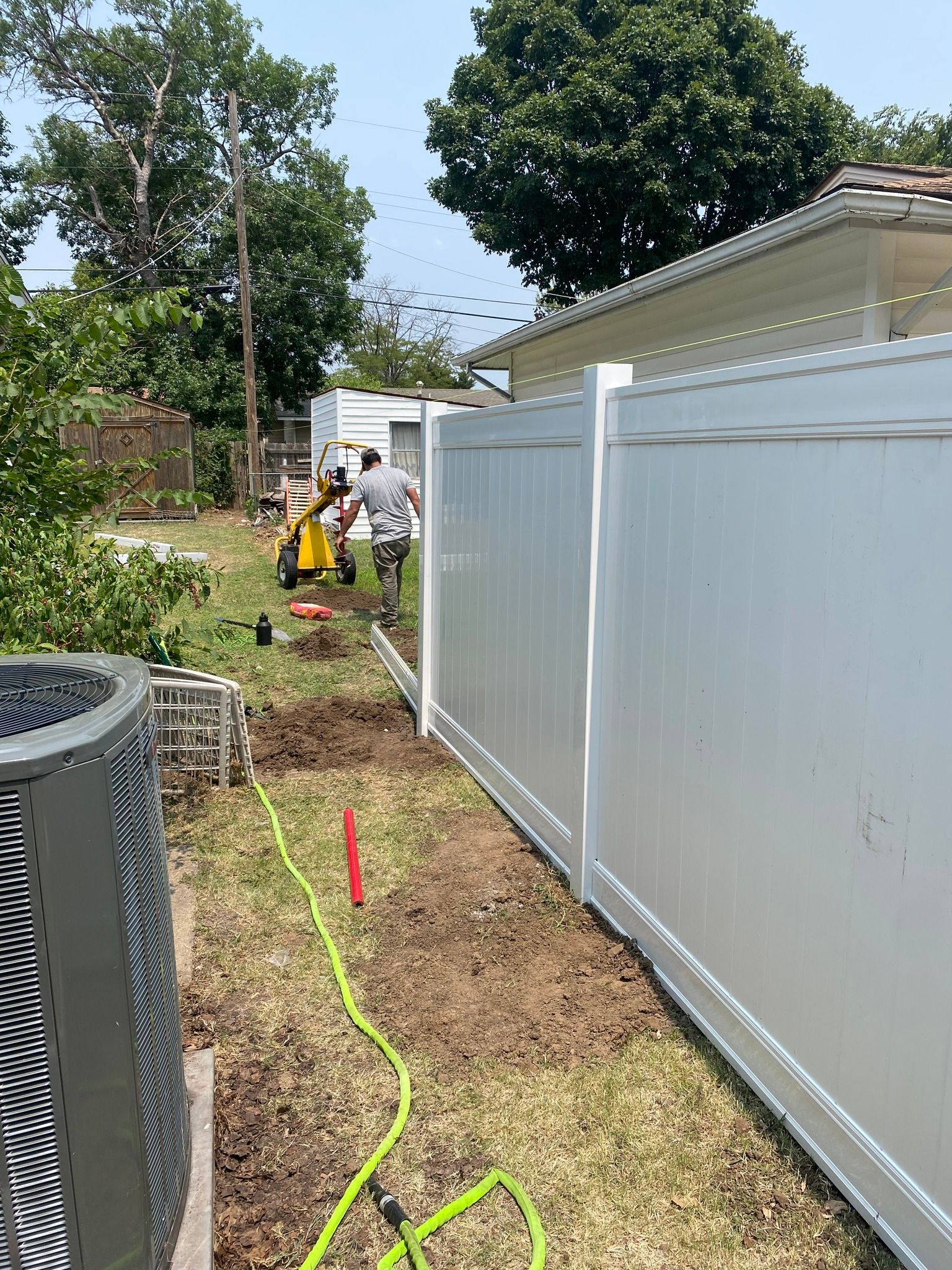 Man installing fence. White fence in yard, with tools and dirt.