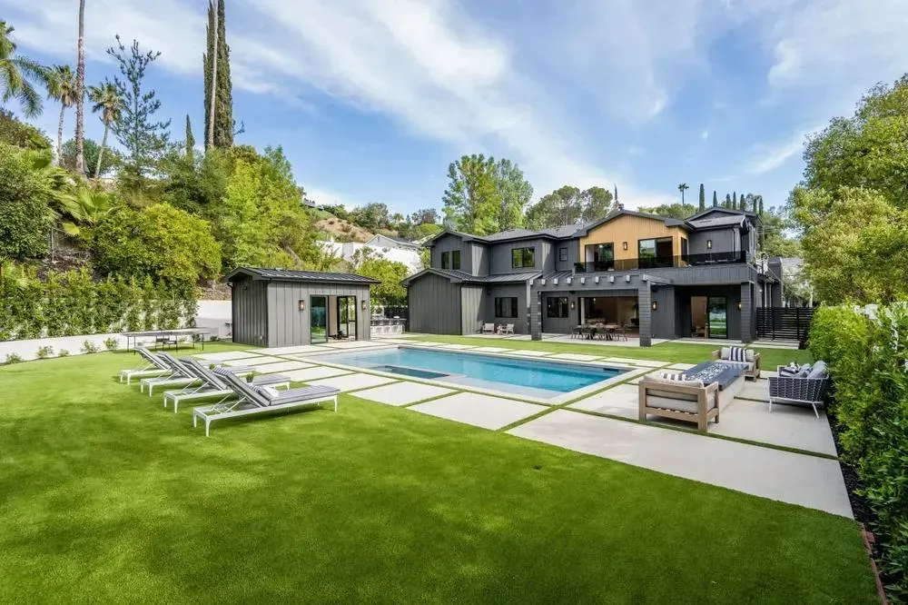 Backyard with pool, luxury home, and manicured green lawn under a blue sky.