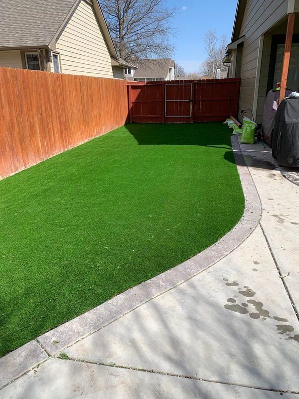 Lush green artificial turf backyard bordered by concrete, red fence.