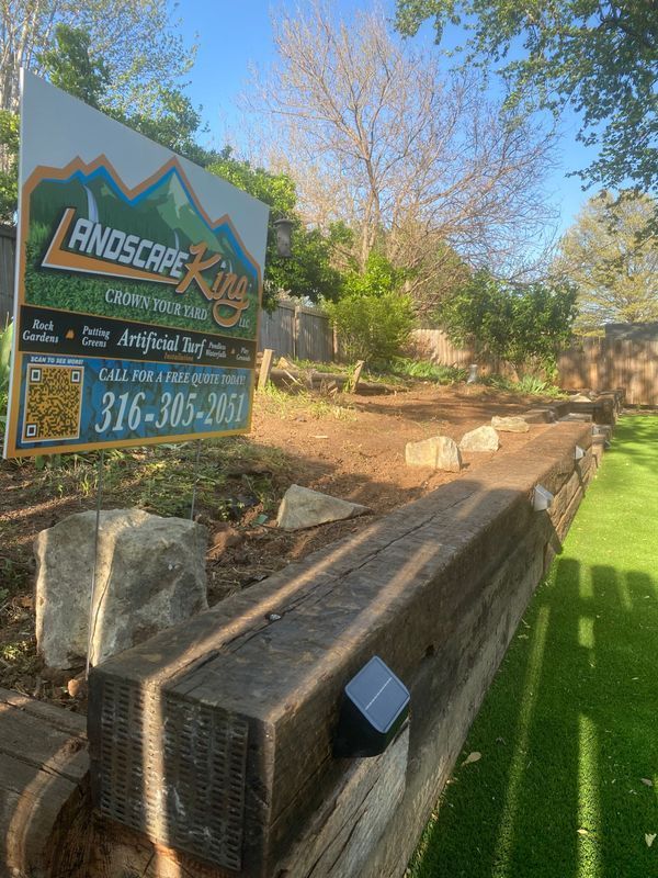 Landscape King sign near a wooden border separating dirt and green turf.