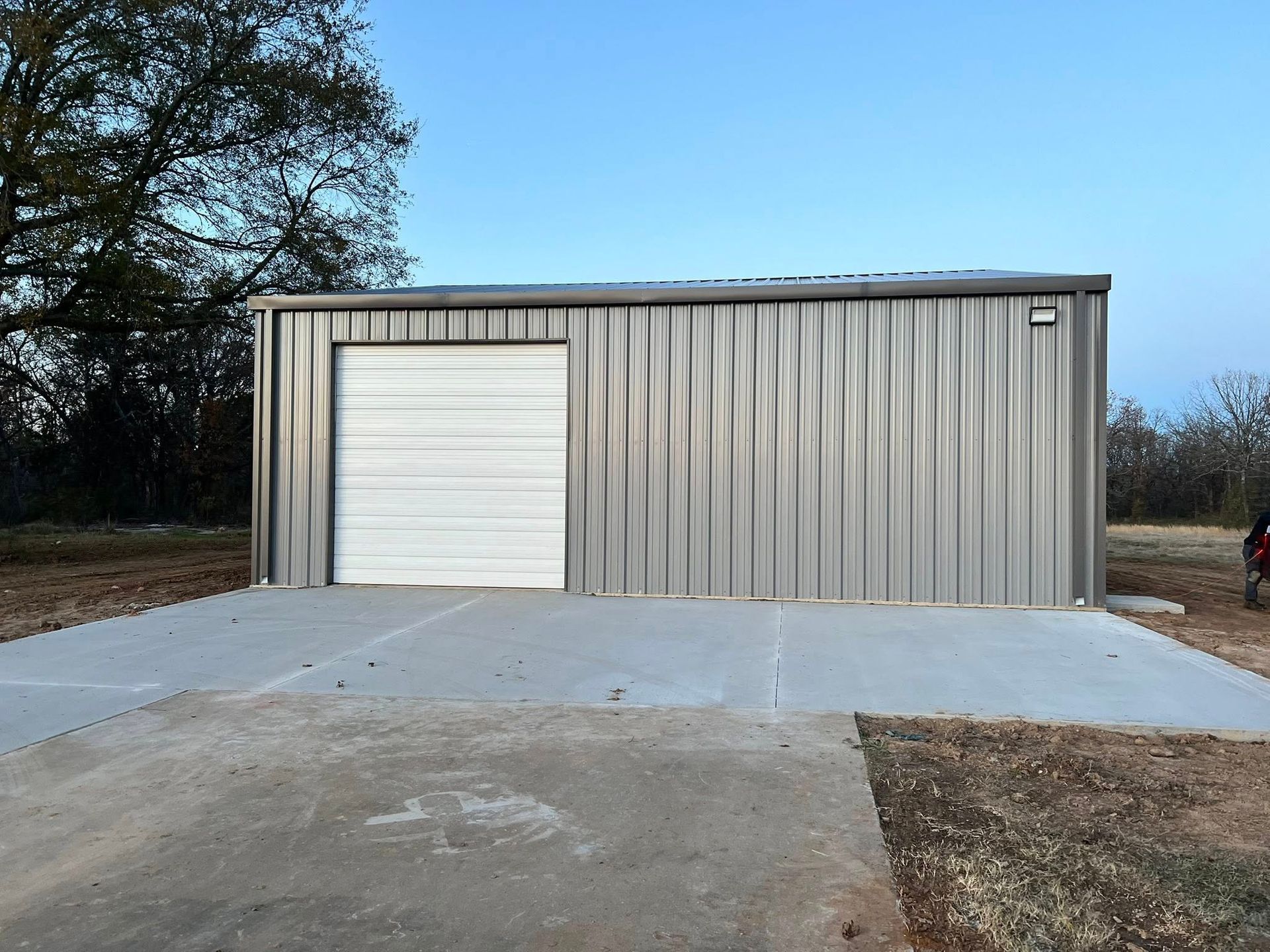 Metal building with a white garage door, on a concrete pad. Blue sky background.