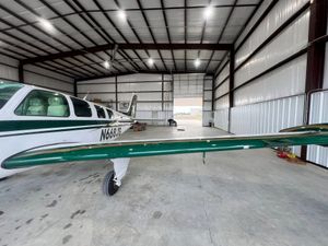 Airplane in hangar with green wing, white fuselage, and open door.